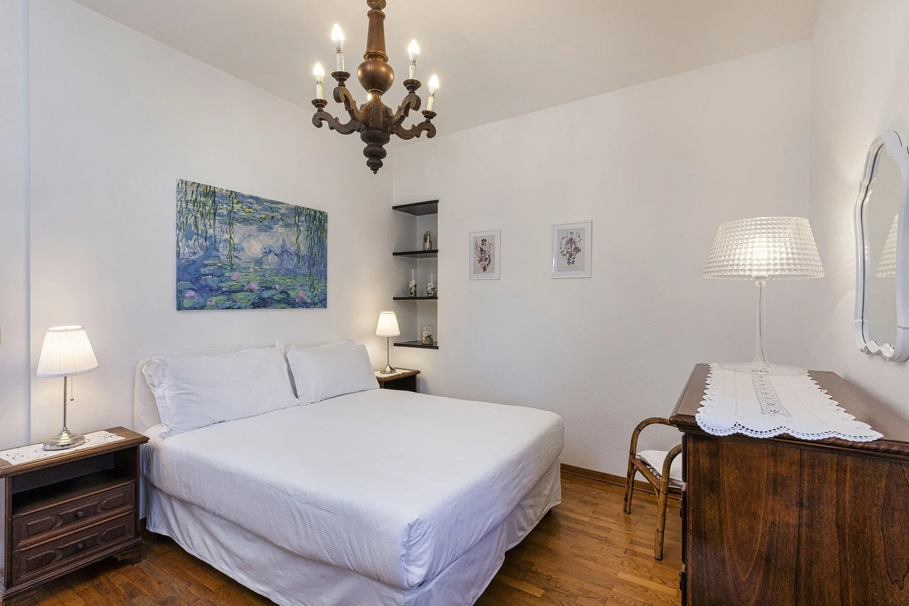 Un dormitorio con una cama bien hecha, cuadros enmarcados y una cómoda de madera.
