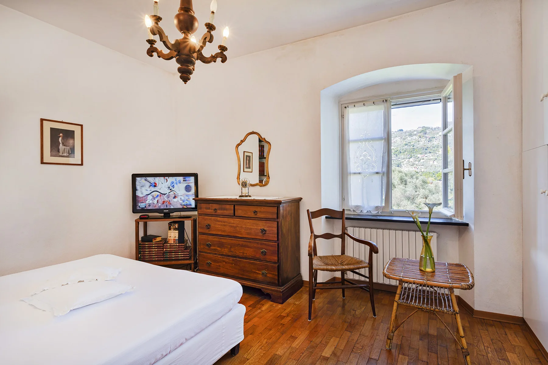 Un dormitorio con una cama, una cómoda de madera y una ventana abierta con vistas a la vegetación.