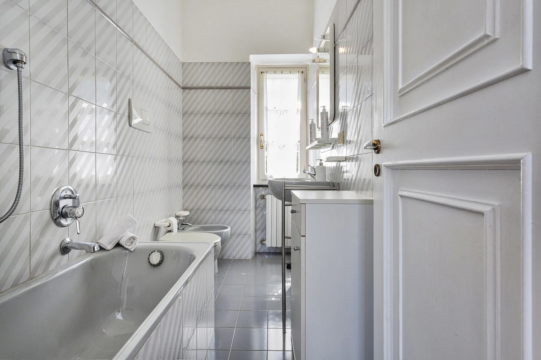 Un baño alicatado con bañera y lavabo junto a una ventana luminosa.