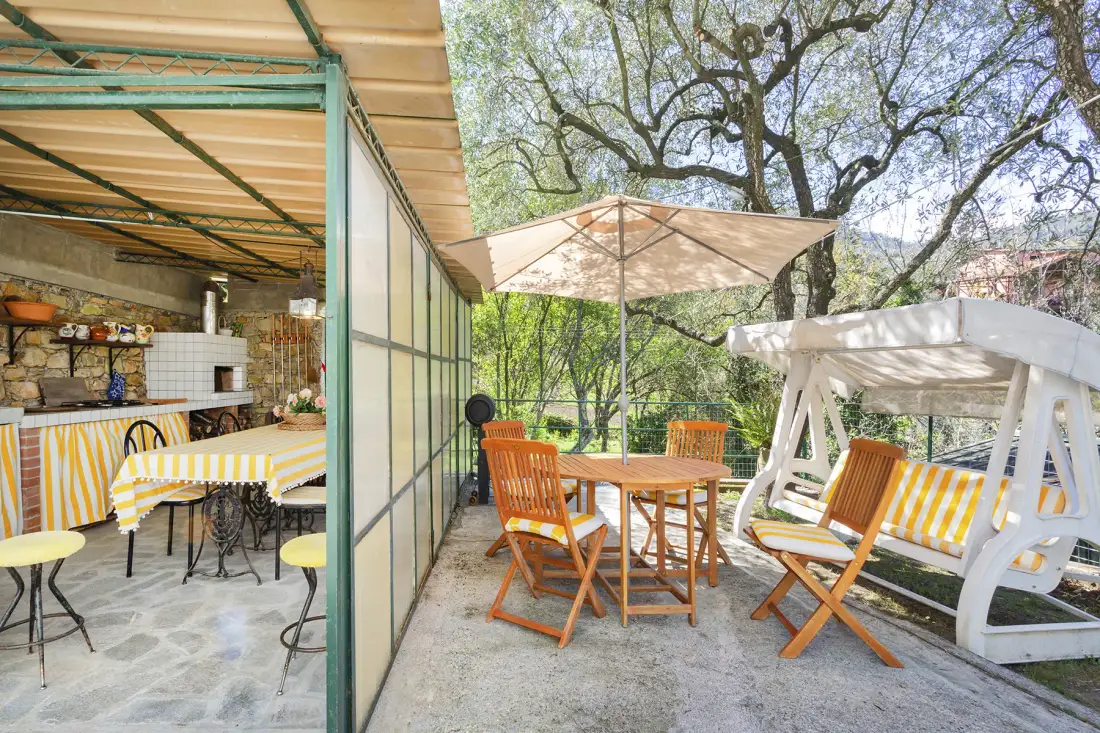 Un patio comedor al aire libre con una mesa, asientos de madera y una gran sombrilla.