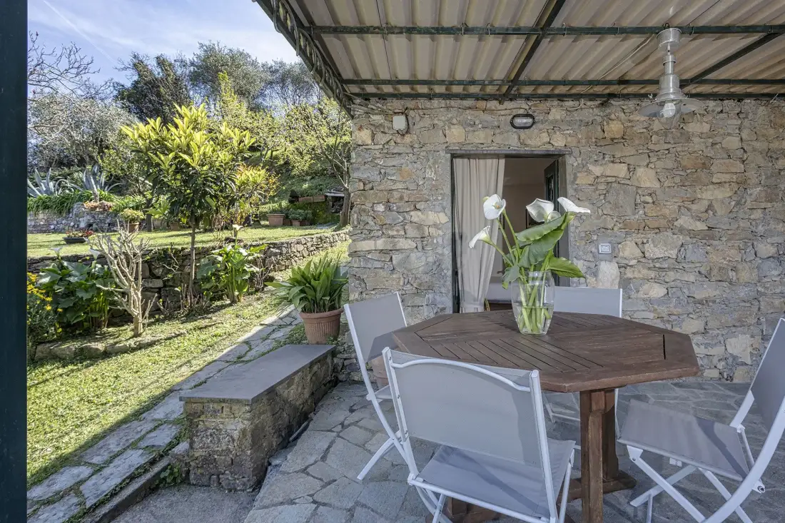 Zona de comedor en un patio de piedra, con mesa y sillas bajo un techo cubierto.