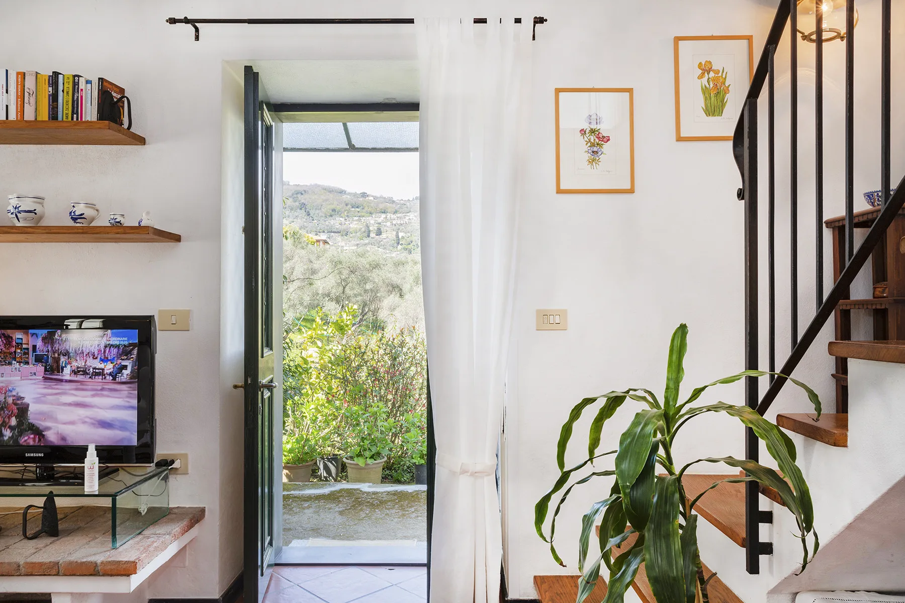 Una sala luminosa se abre a un balcón por puertas de vidrio, con una escalera cerca.