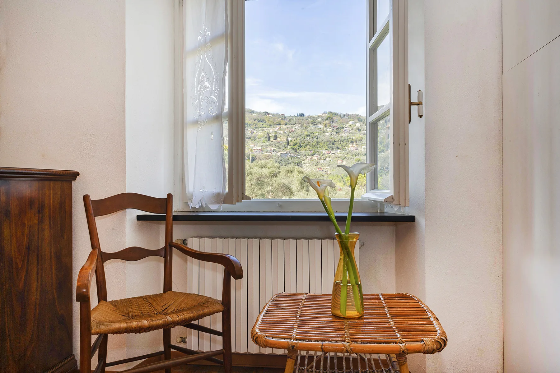 Una habitación luminosa con una ventana abierta que da a una ladera verde.