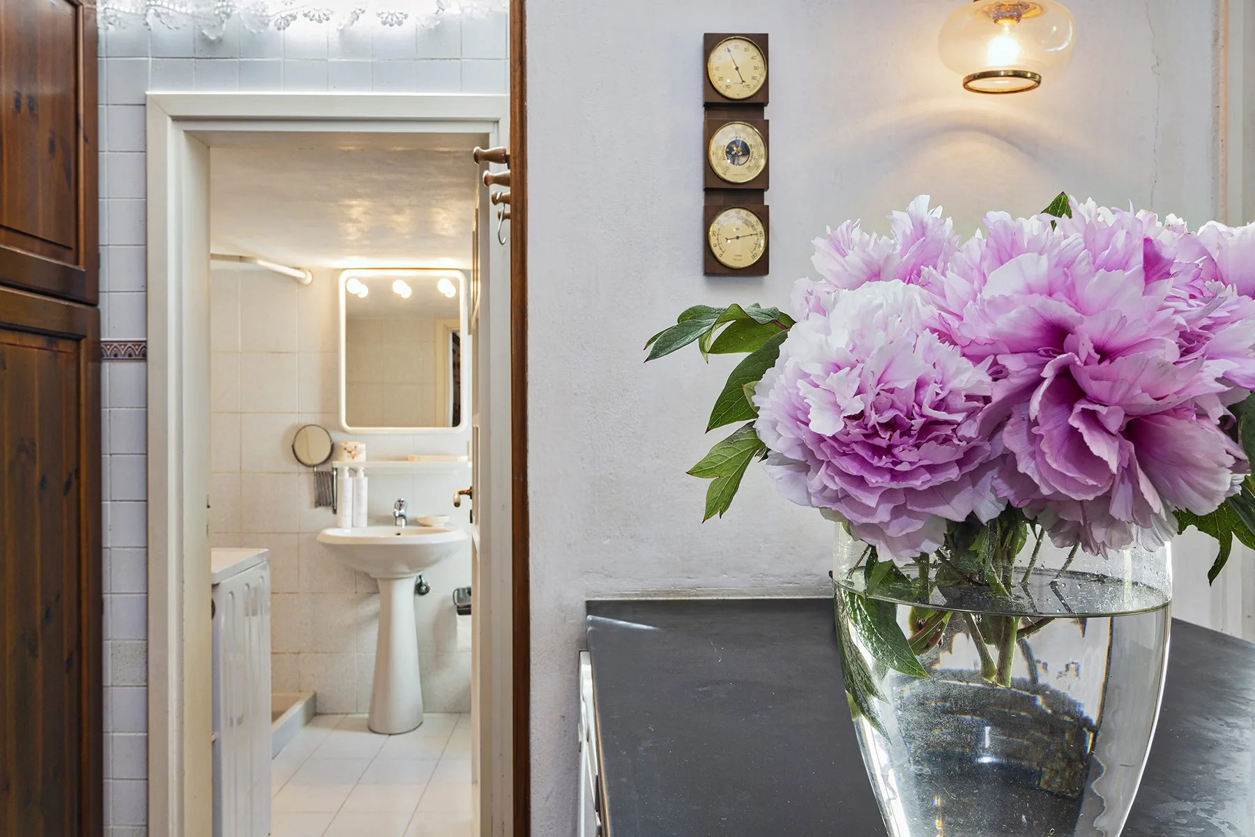 Un jarrón con flores rosas está sobre una mesa junto a una puerta abierta que da a un baño.