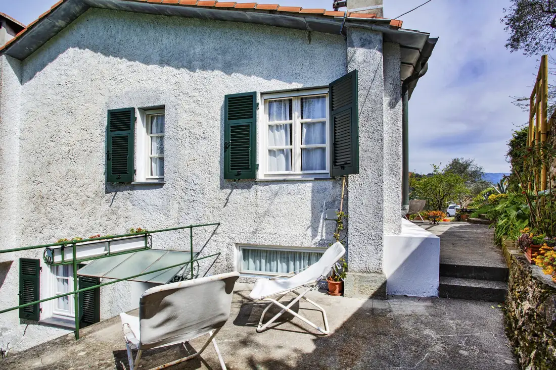 Una casa blanca de estuco con contraventanas oscuras da a un patio soleado.