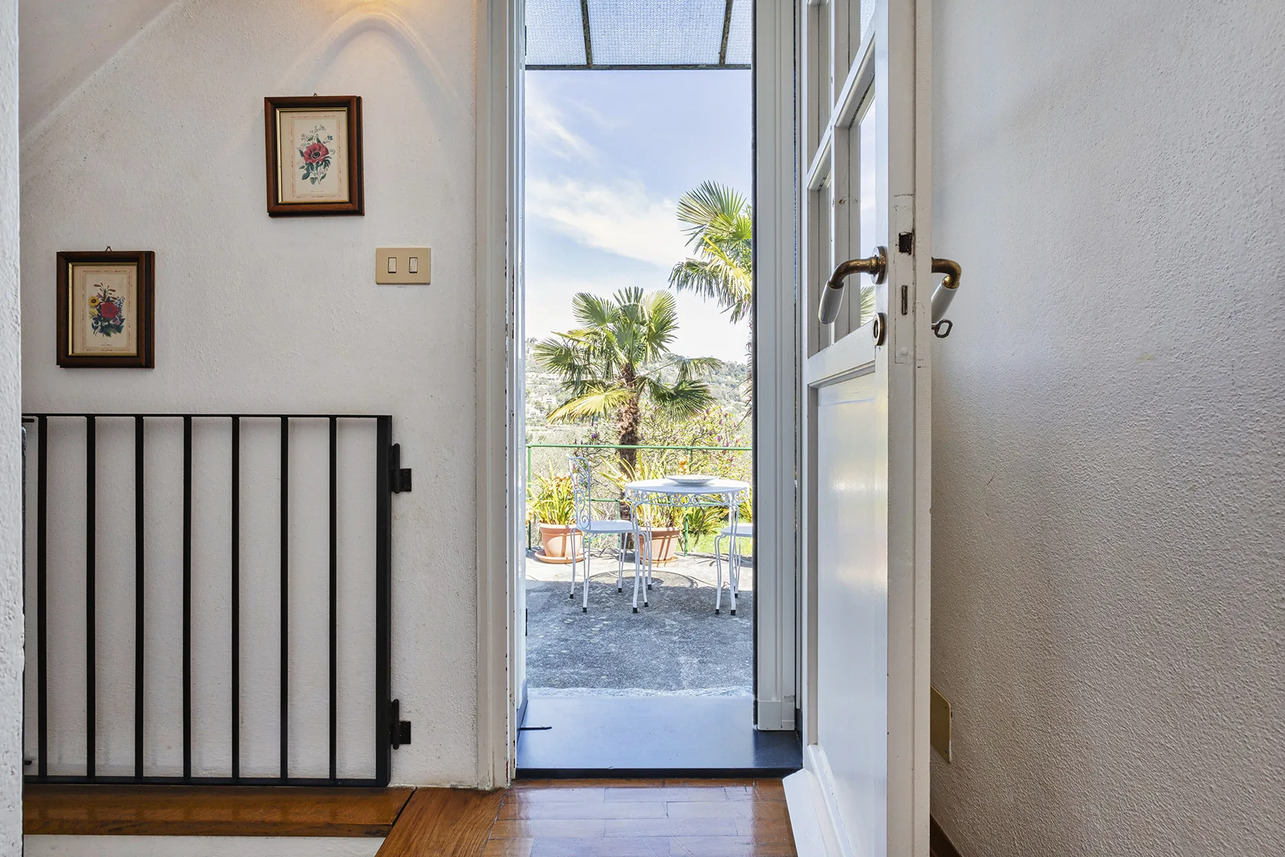 Una puerta abierta da a una terraza con asientos al aire libre y palmeras.