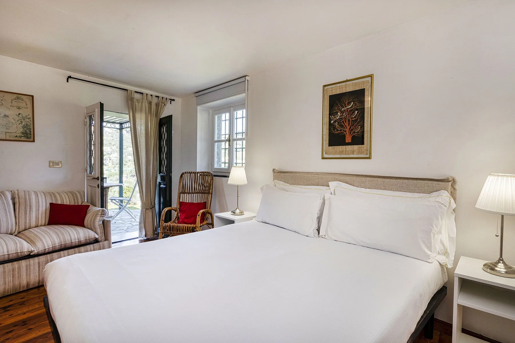 Un dormitorio luminoso con una cama grande, asientos a rayas y ventanas con vistas a la vegetación.
