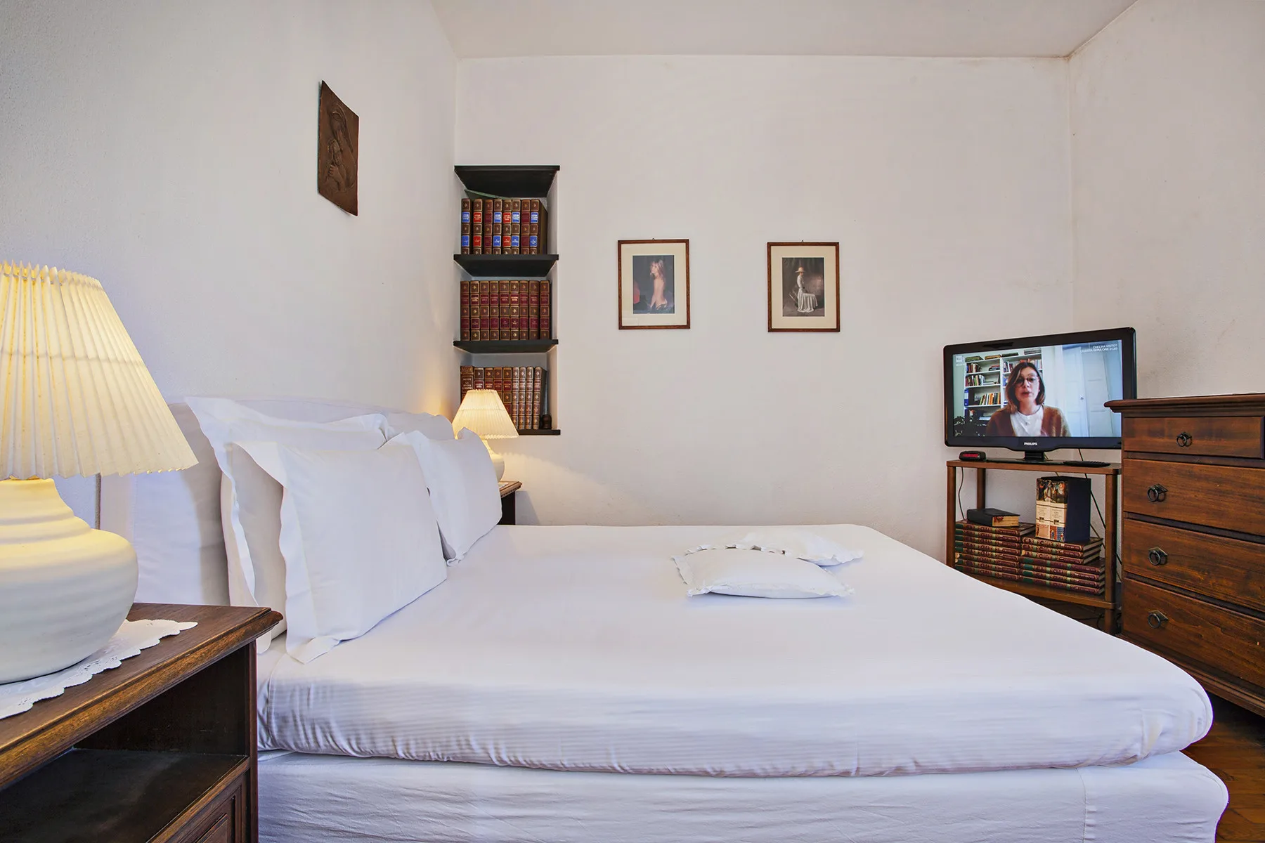 Un dormitorio con una cama bien arreglada y un televisor sobre una cómoda de madera.