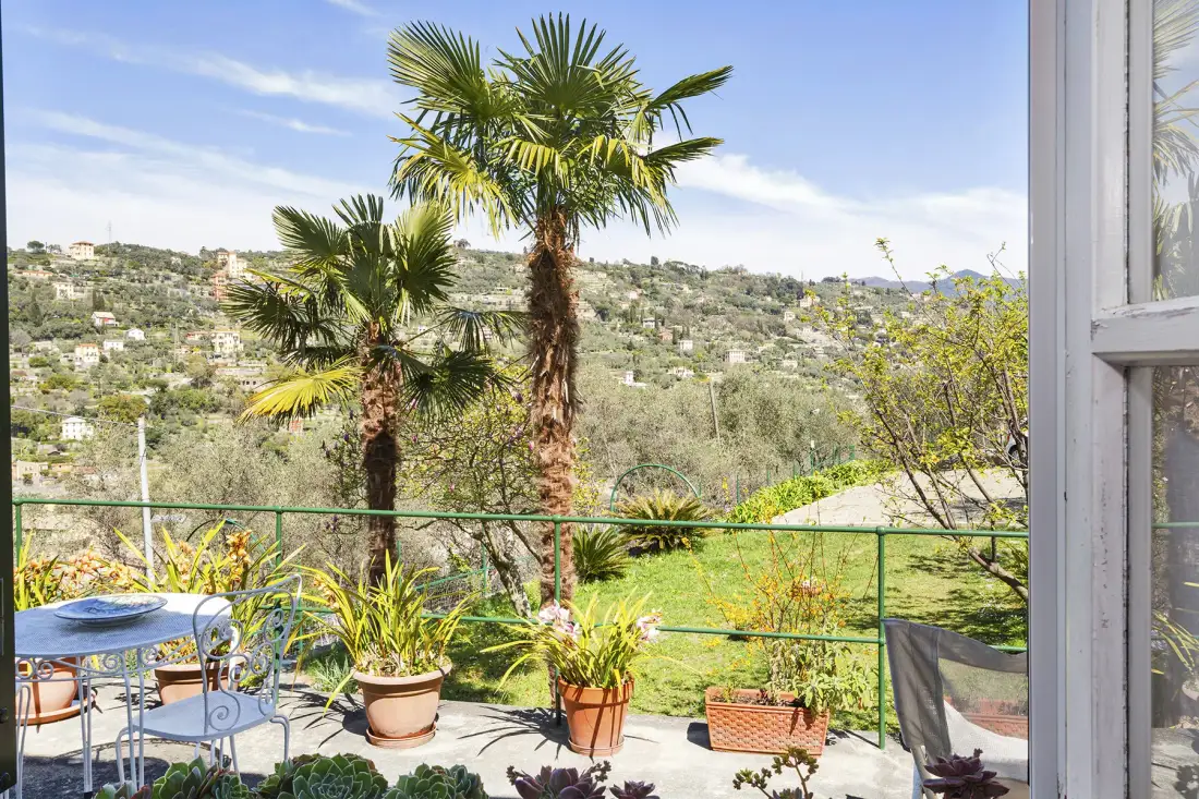 Un patio con asientos al aire libre y plantas en macetas da a una ladera verde.