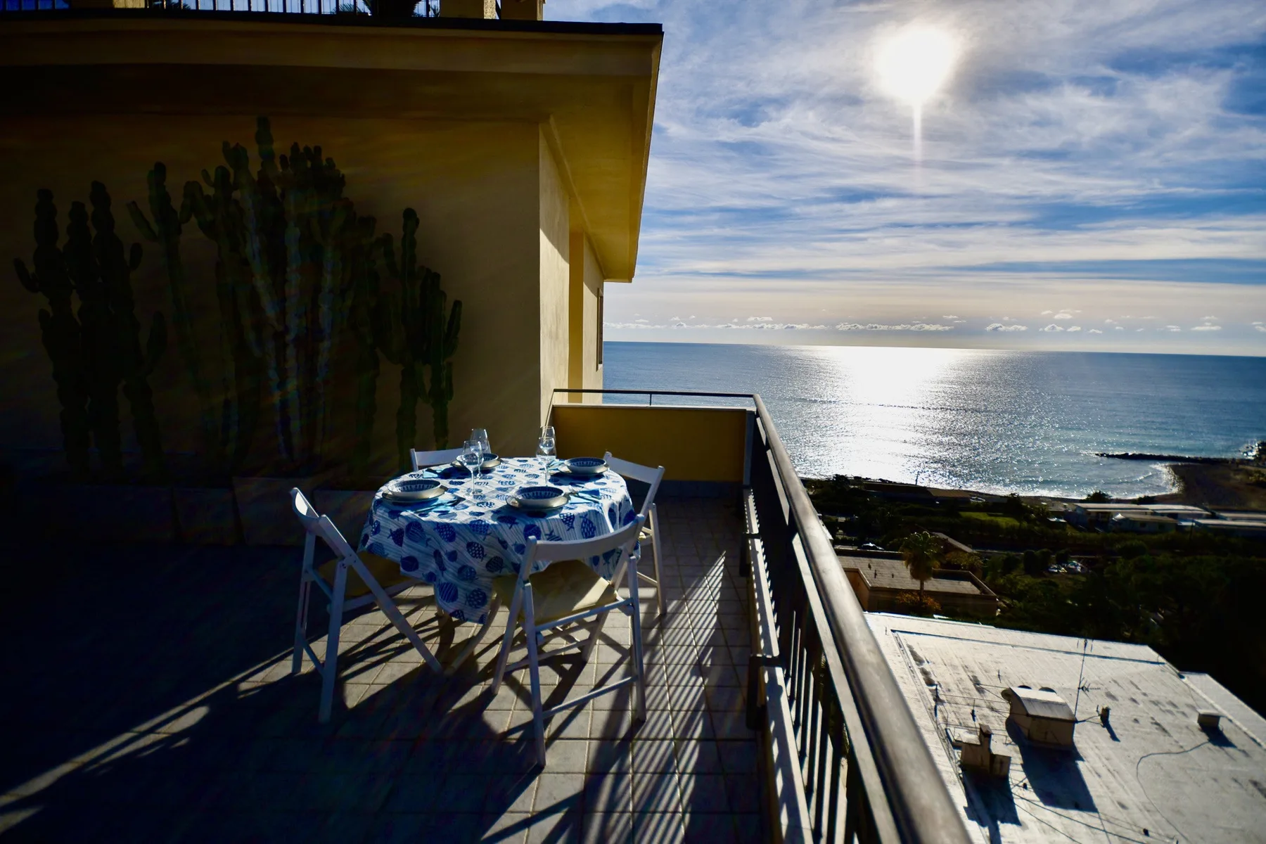 Un balcón con una mesa pequeña da al mar bajo un sol brillante.