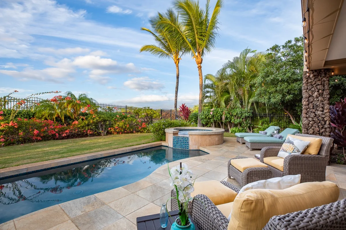 Una piscina exterior y asientos en el patio están rodeados de plantas tropicales y palmeras.