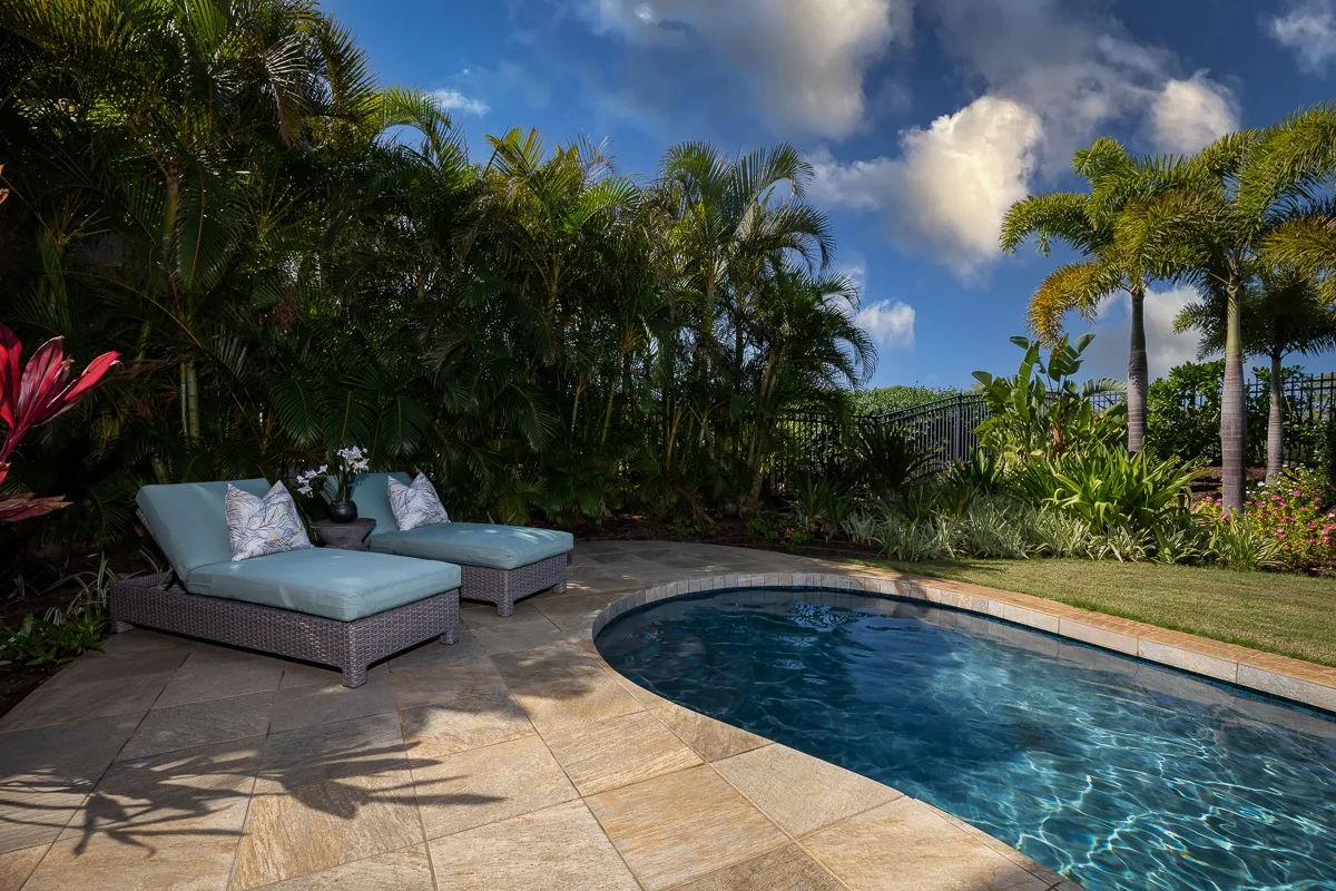 Una piscina al aire libre junto a asientos acolchados y vegetación tropical.
