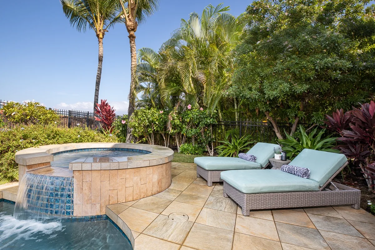 Un patio ajardinado cuenta con un jacuzzi circular elevado y asientos acolchados.