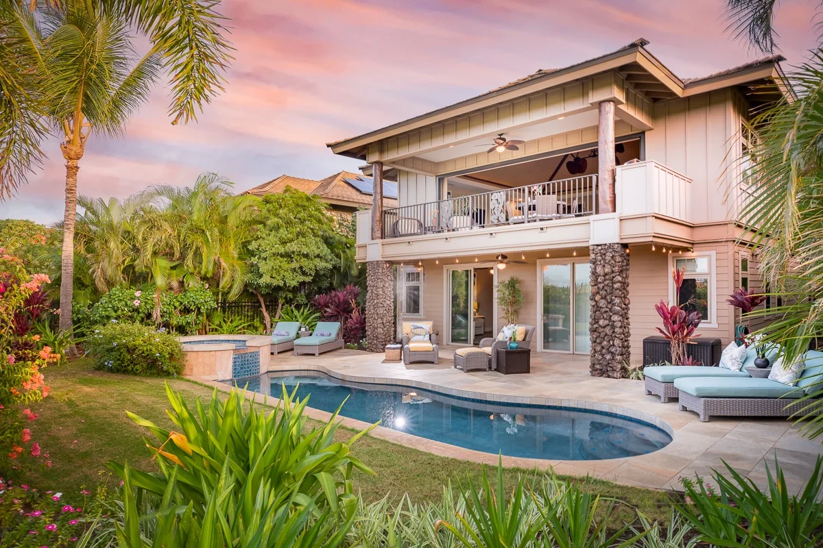 Una casa de dos plantas da a una piscina rodeada de vegetación tropical.