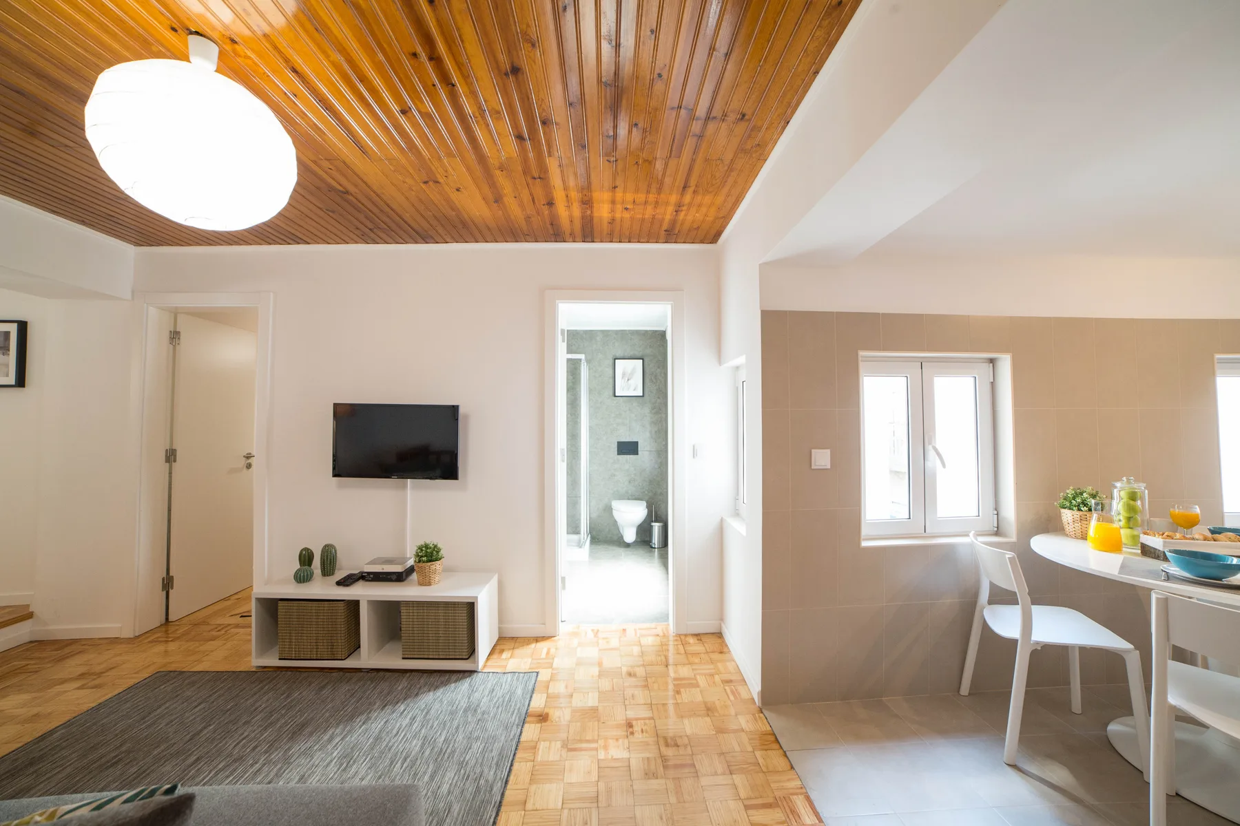 A bright living and dining area with a television, table, and wood-paneled ceiling.
