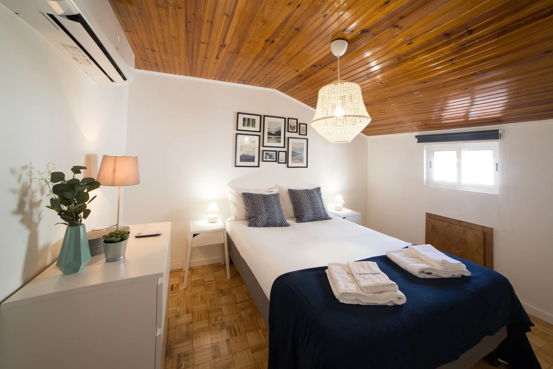 A bedroom with a double bed, framed pictures, and a wooden ceiling.