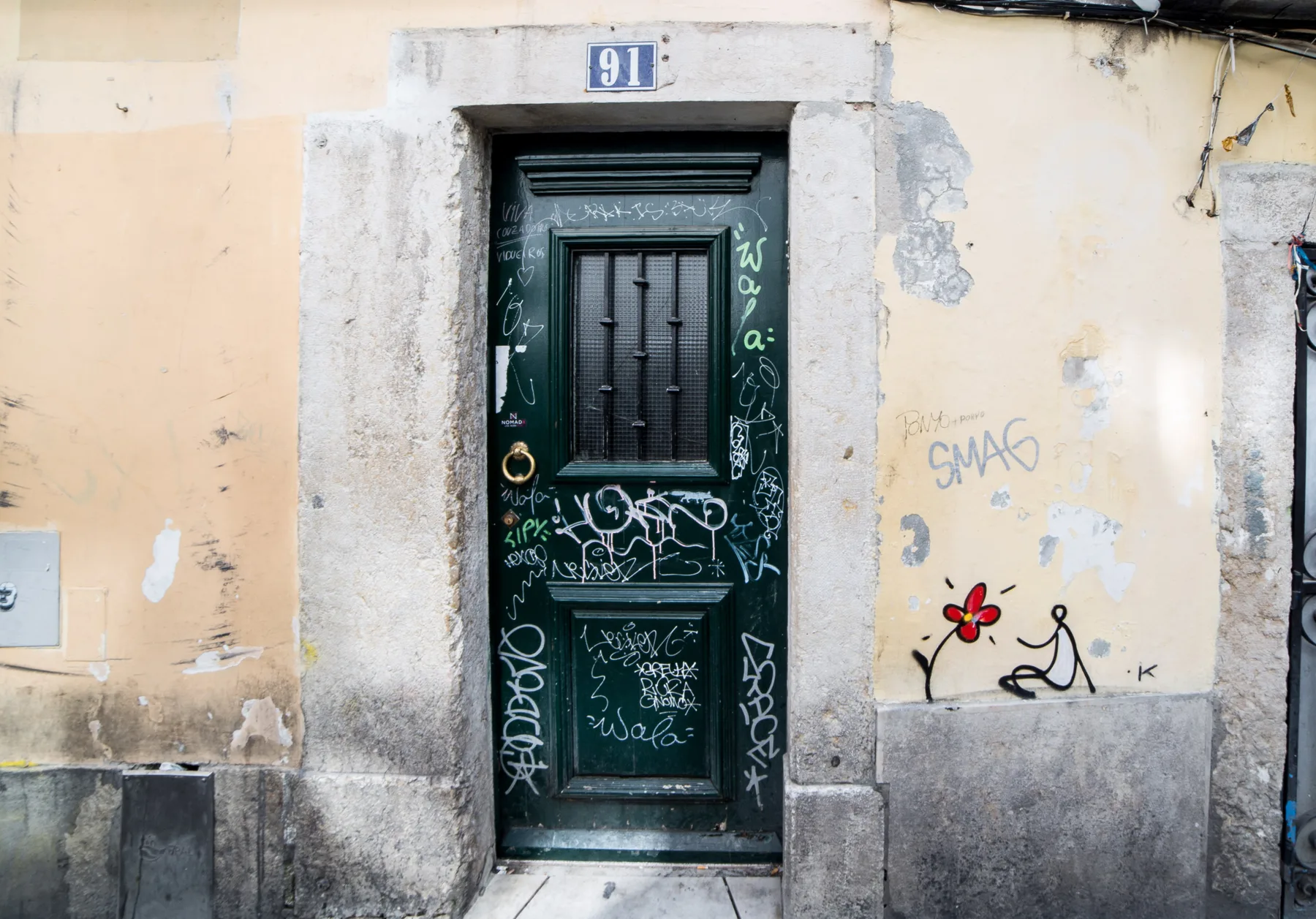 A dark green entrance door covered in graffiti is set into a worn facade.