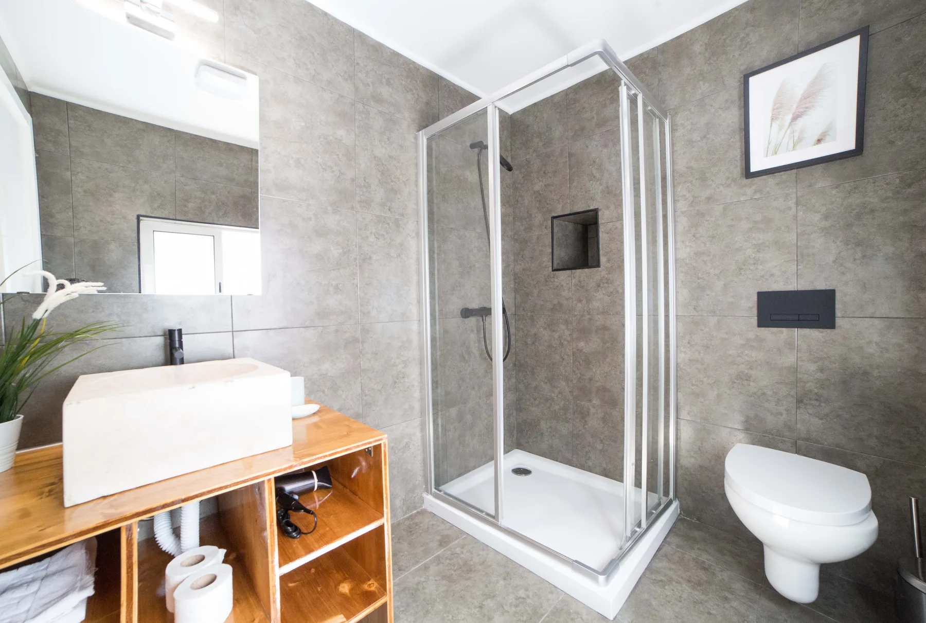 A tiled bathroom with a glass shower, wall-mounted sink, and toilet.
