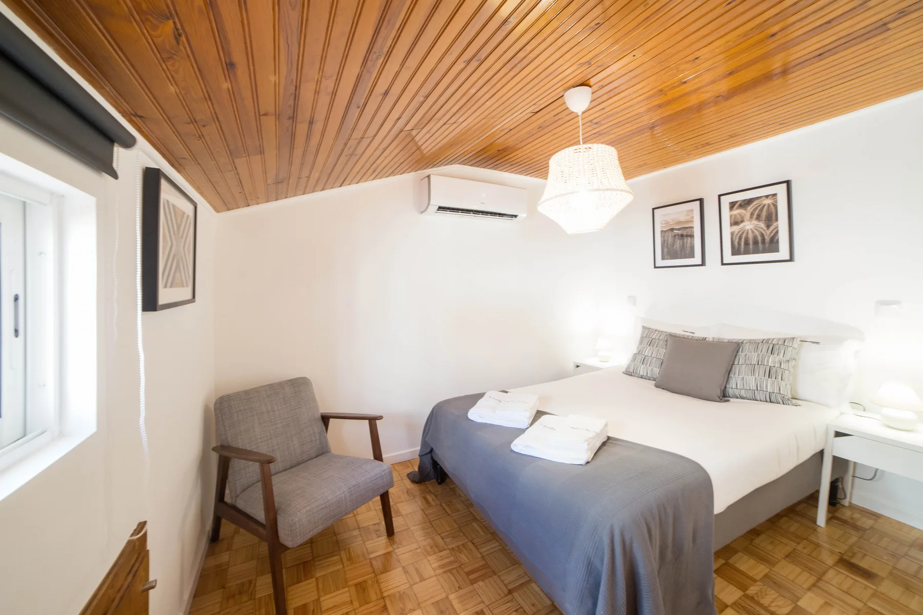 Un dormitorio con una cama, una mesita de noche y un sillón bajo un techo de madera.