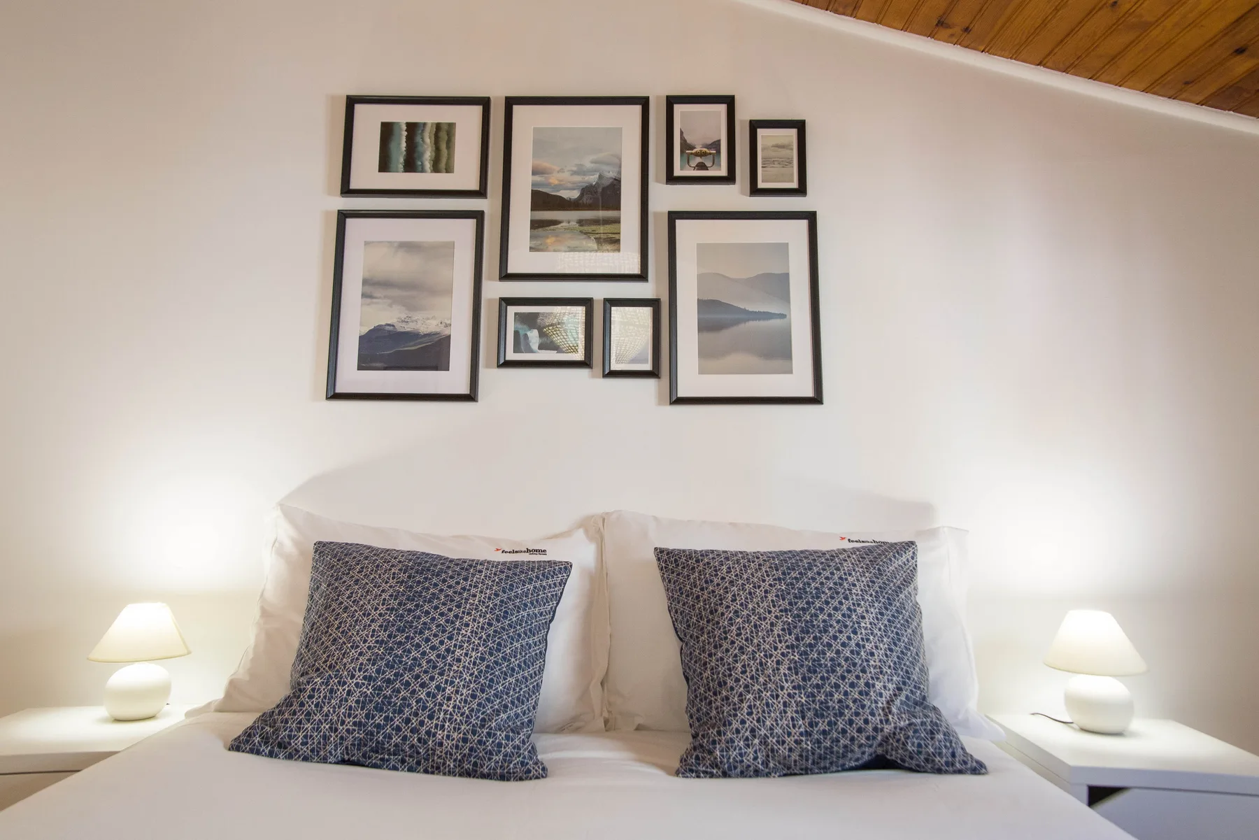A bedroom with two patterned pillows beneath a gallery of framed pictures.