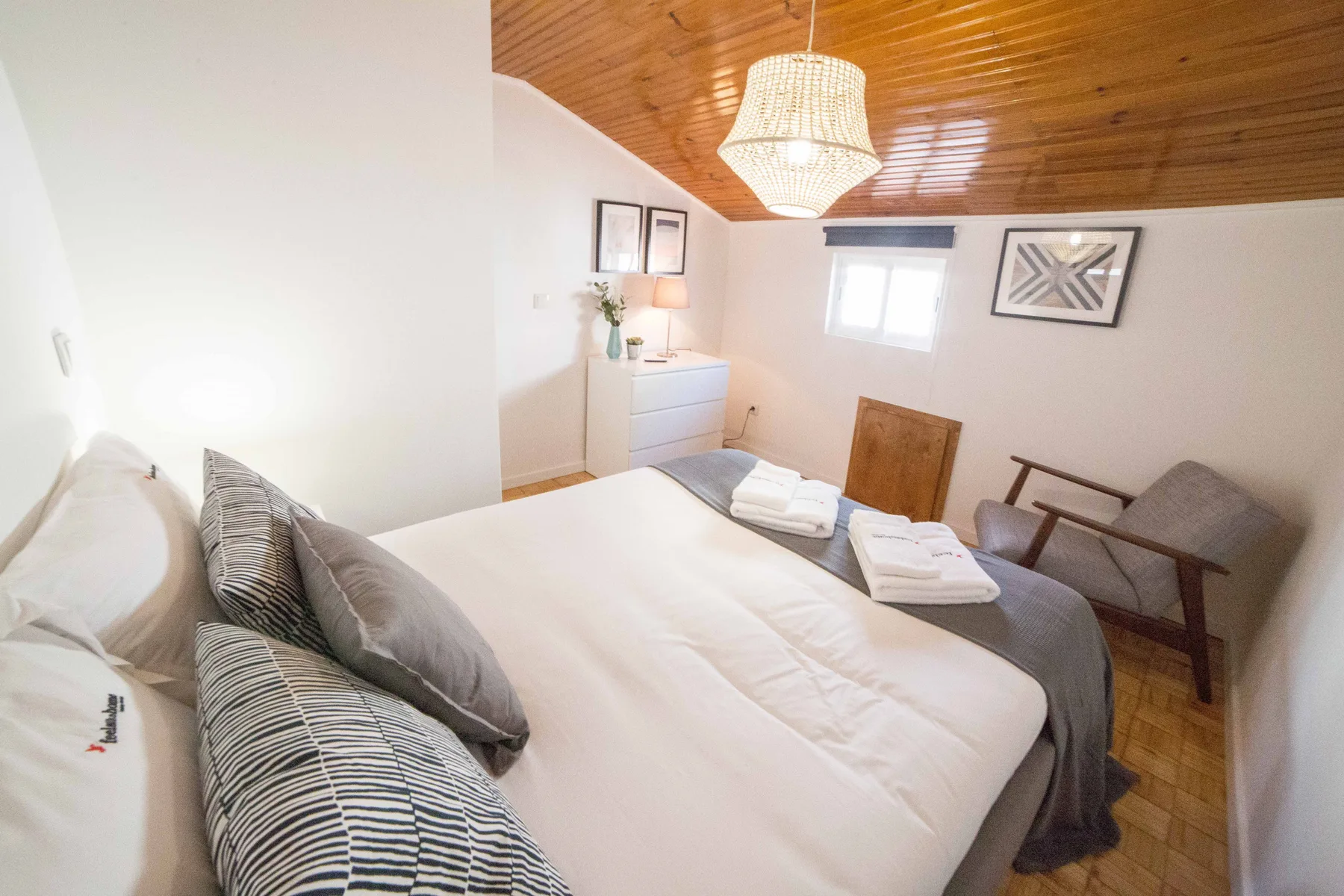 A bedroom with a bed, folded towels, and seating beneath a wood-paneled ceiling.