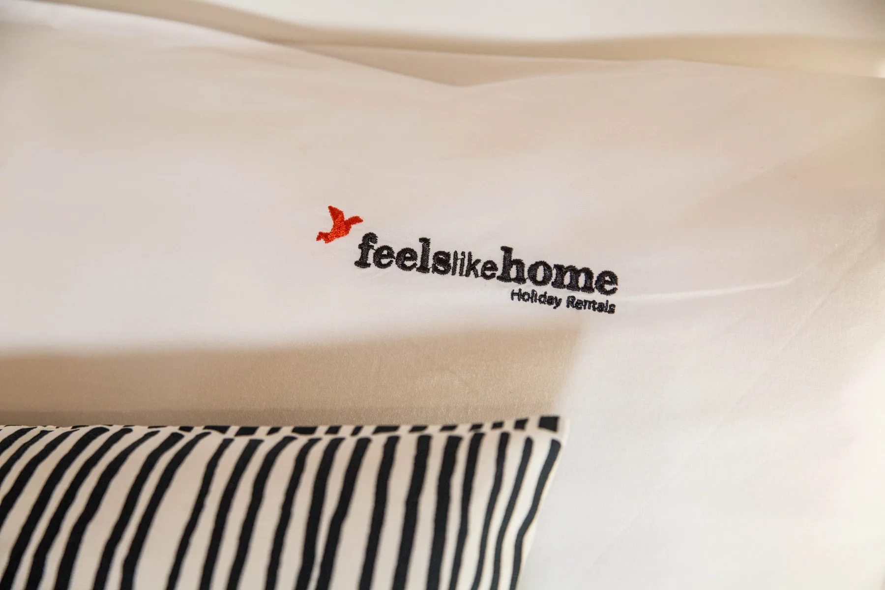 Close-up of a white pillow with a black striped edge and a small printed logo.