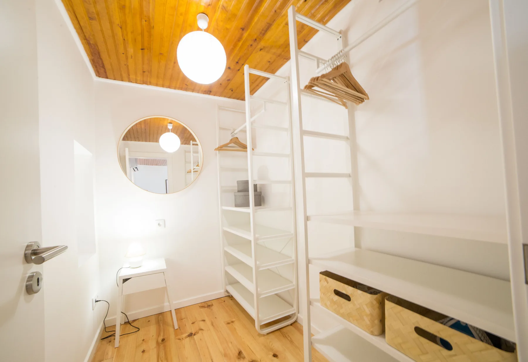 A bright dressing room with open shelving, hanging space, and a wooden ceiling.