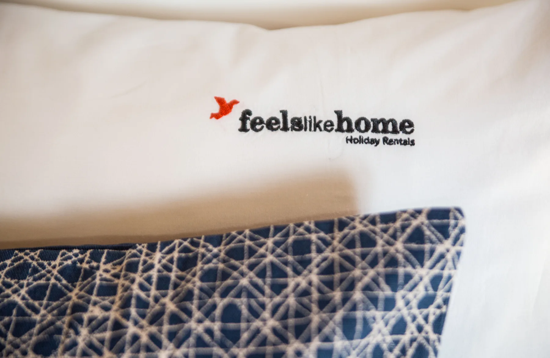 A bed with white linens and a blue patterned blanket.