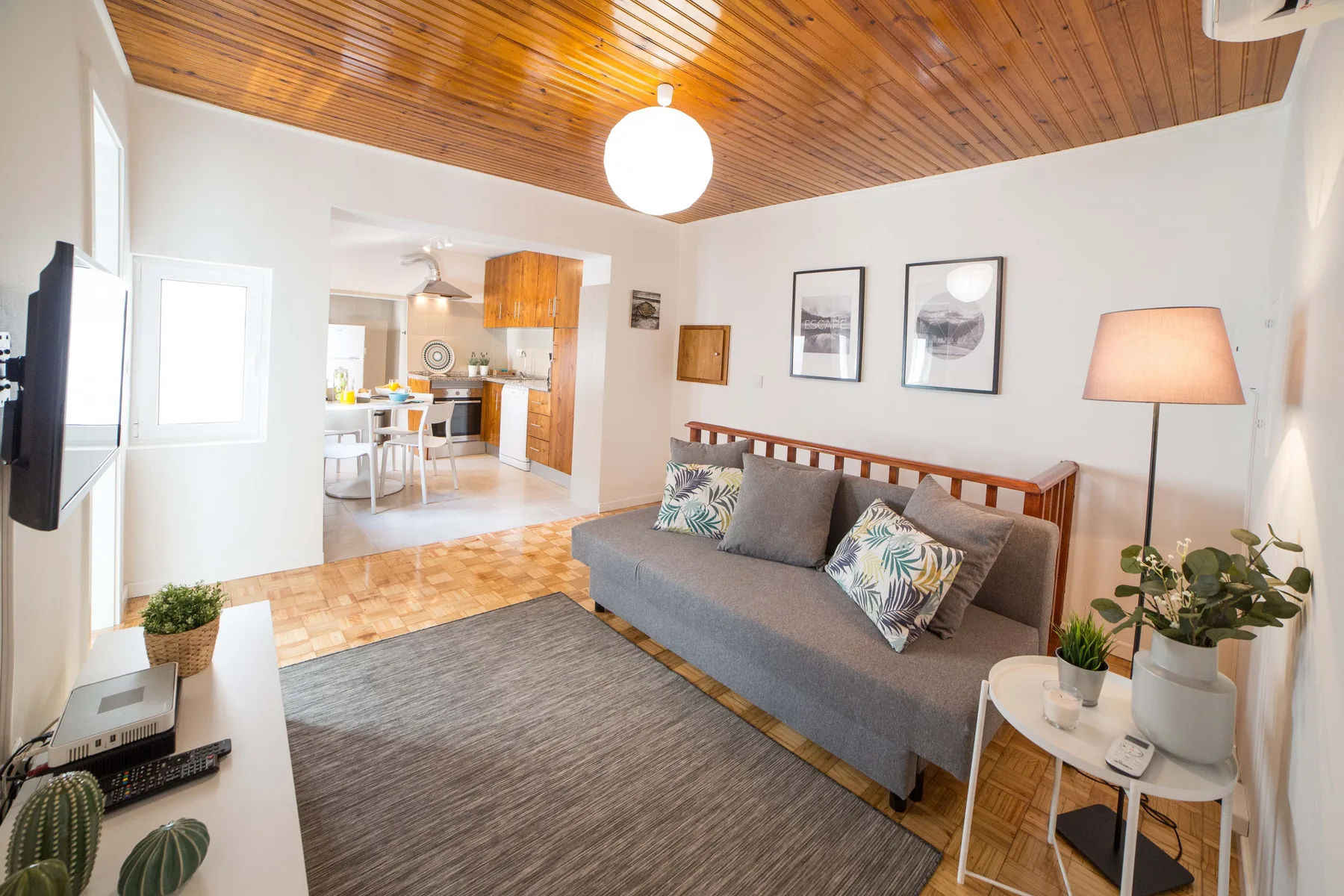 Sala de estar con asientos, techo de madera y cocina contigua.