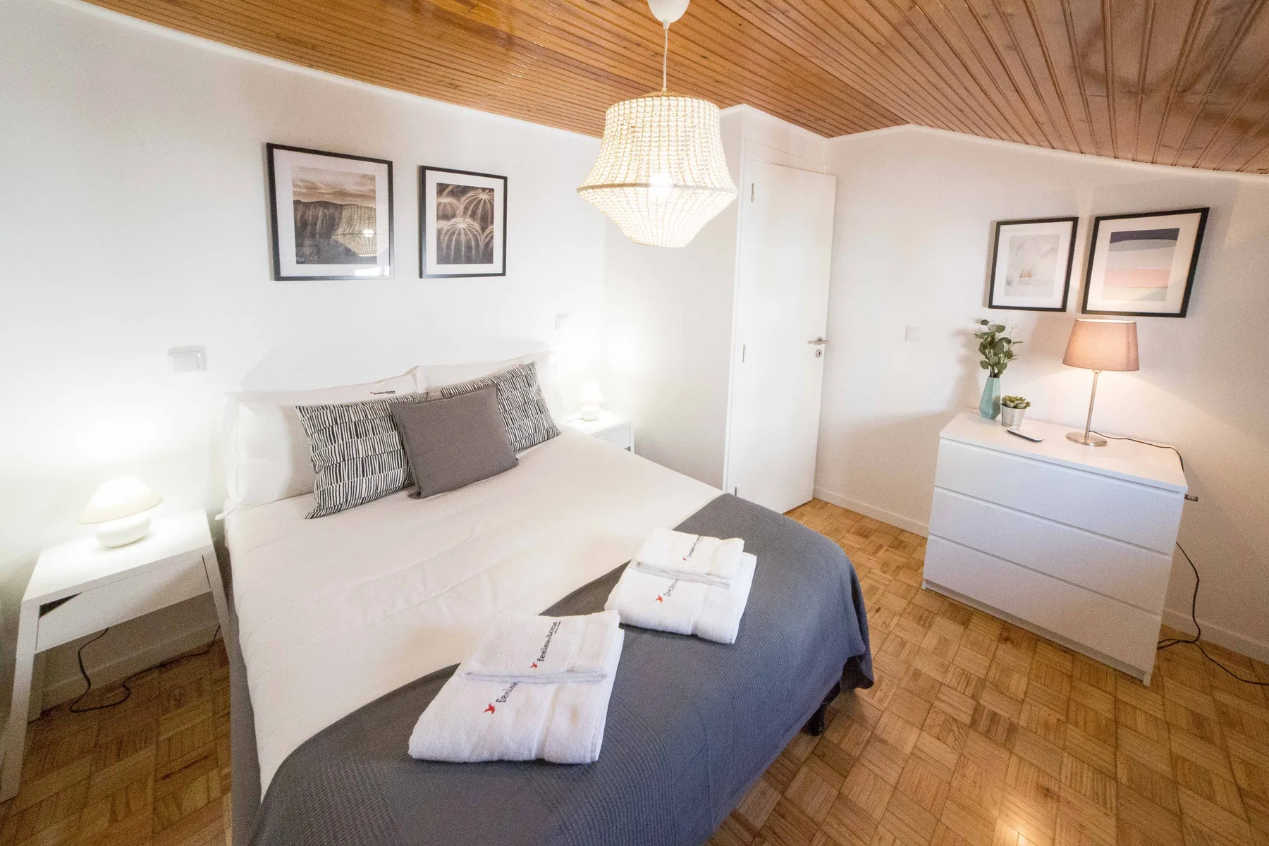 A bedroom with a neatly made bed, bedside tables, and framed wall art.