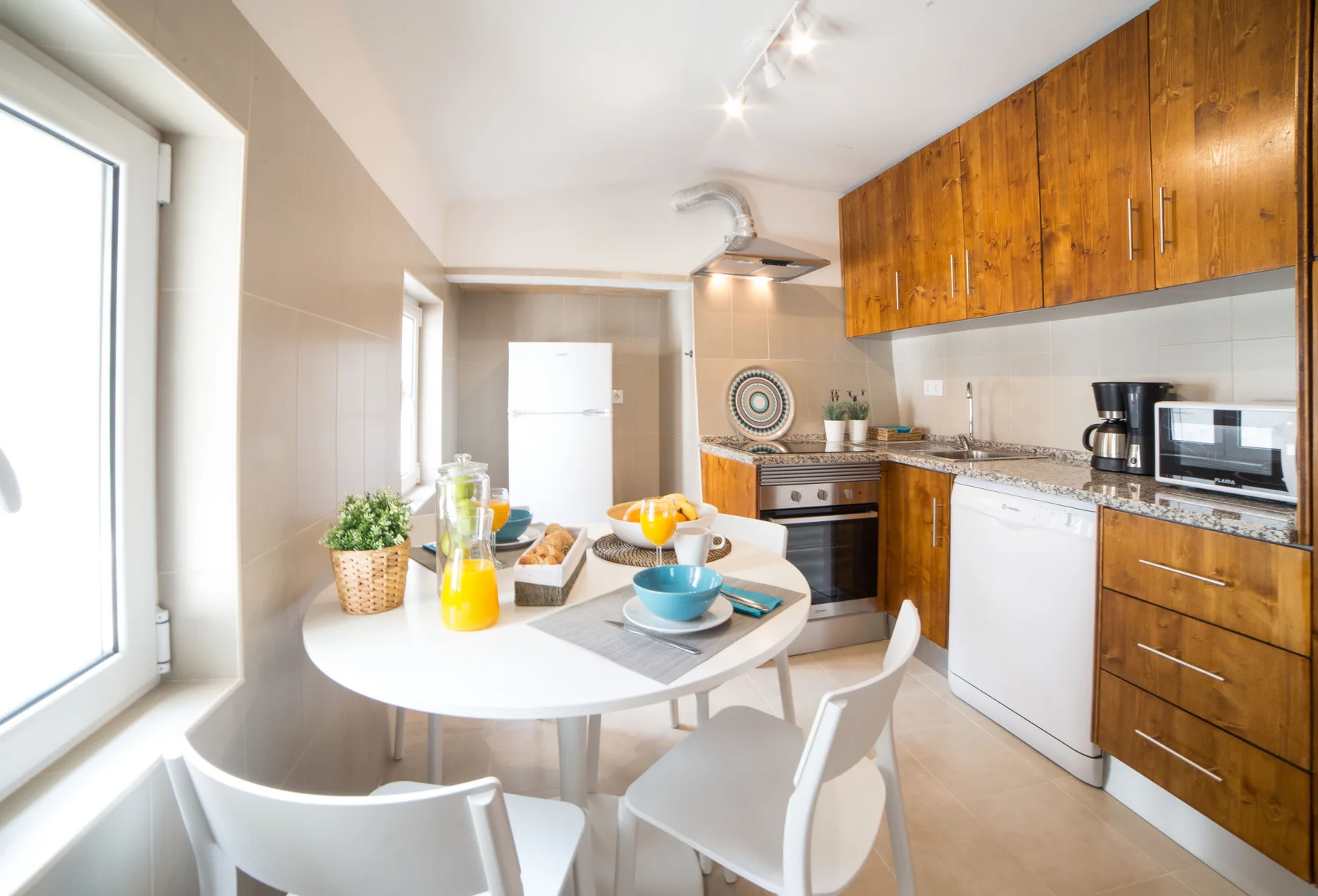 Una cocina luminosa con zona de comedor y una mesa redonda junto a armarios de madera.