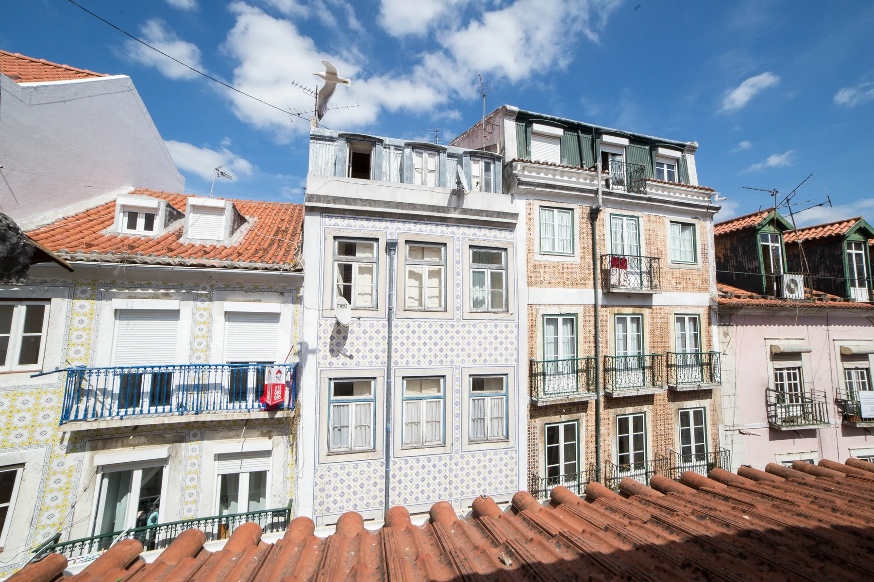 A row of colorful apartment buildings with tiled roofs beneath a partly cloudy sky.