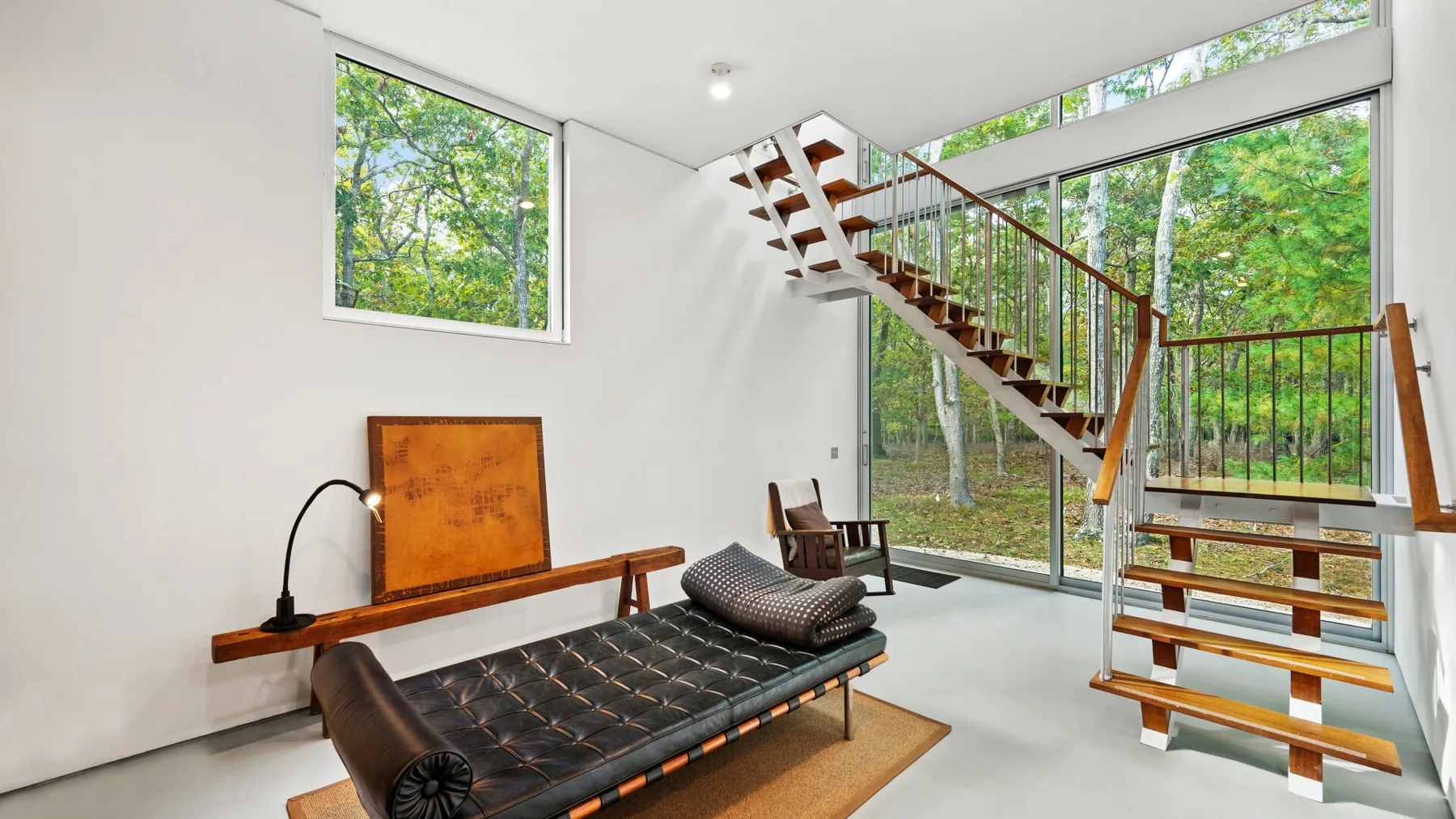 A bright living area with a low seating piece beside a staircase and large windows.
