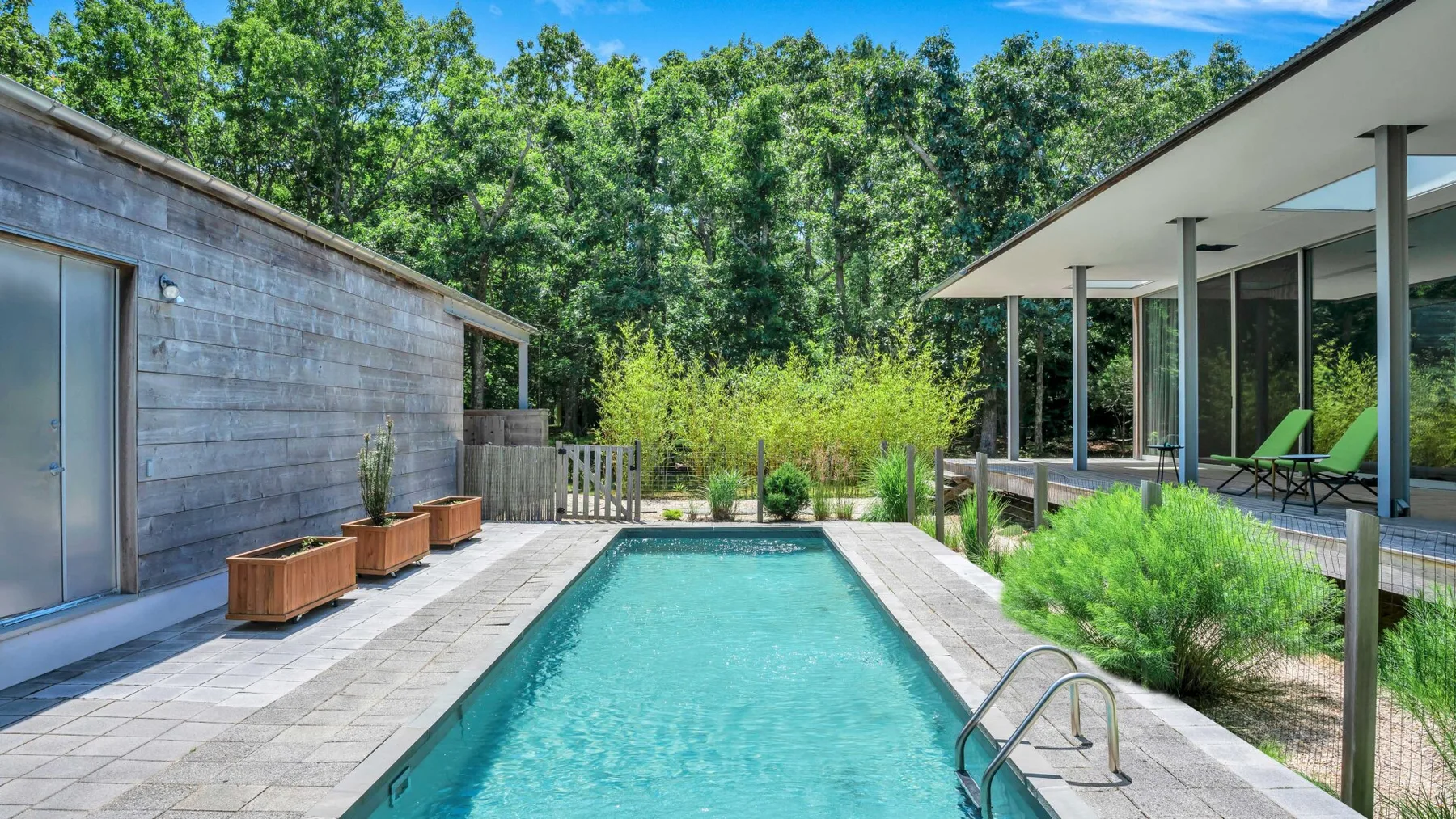 An outdoor swimming pool sits between a wood-sided building and a covered patio.
