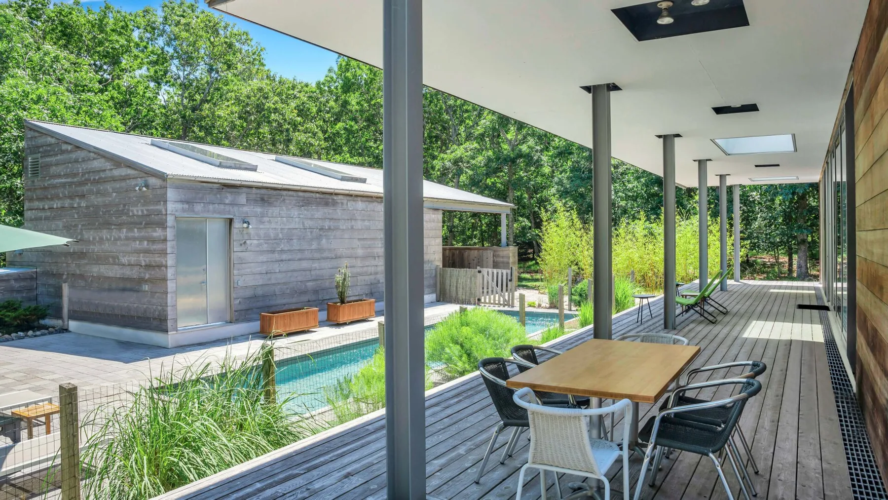 Una terraza exterior cubierta tiene una mesa de comedor junto a una piscina.
