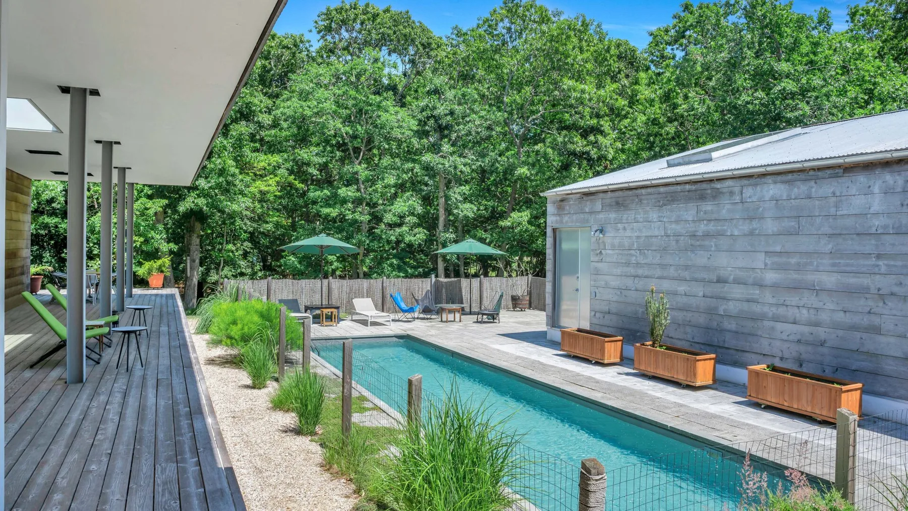 An outdoor swimming pool sits beside a deck, with trees and seating nearby.
