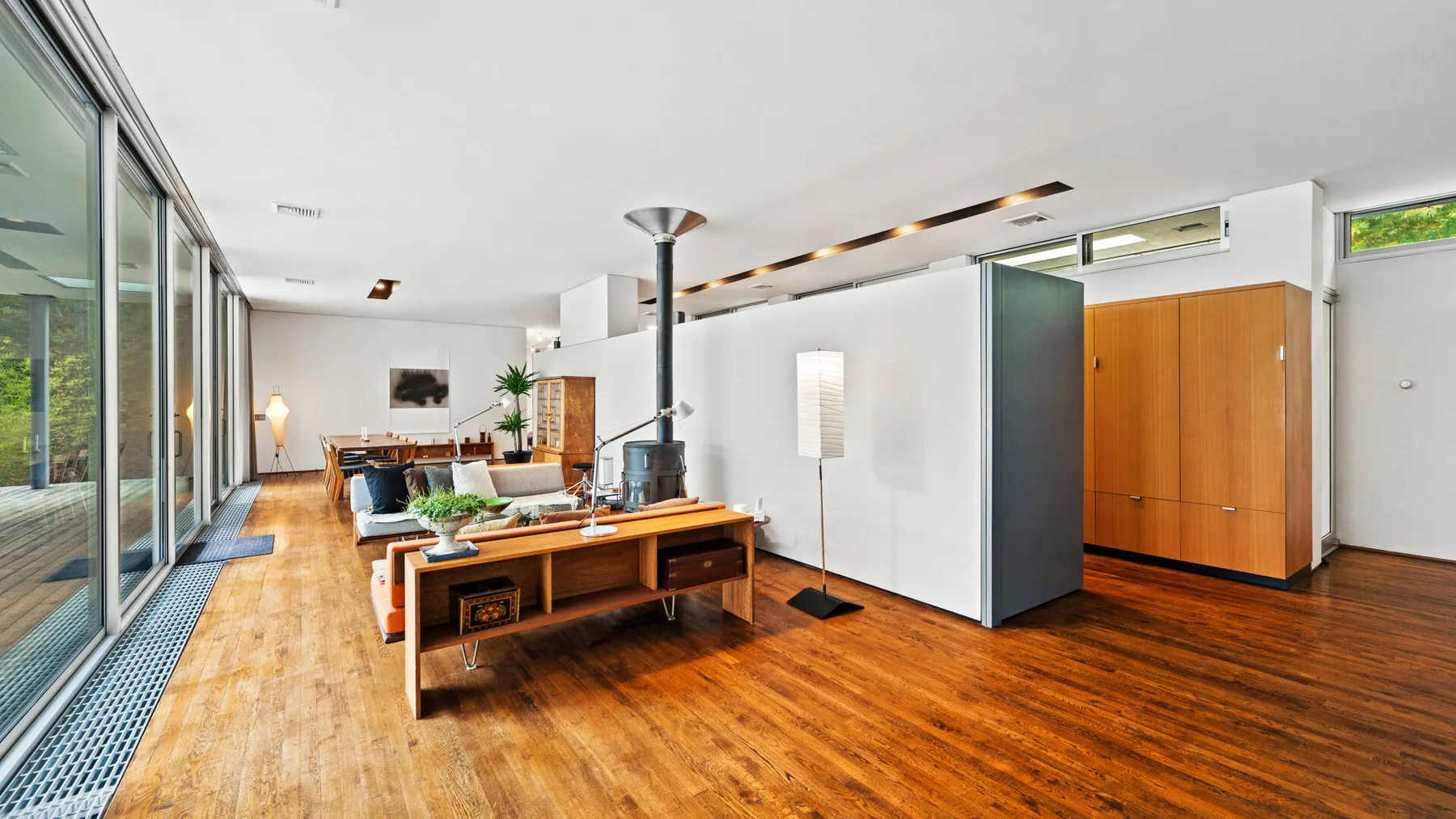 A bright modern living room with a long wooden table and large glass windows.