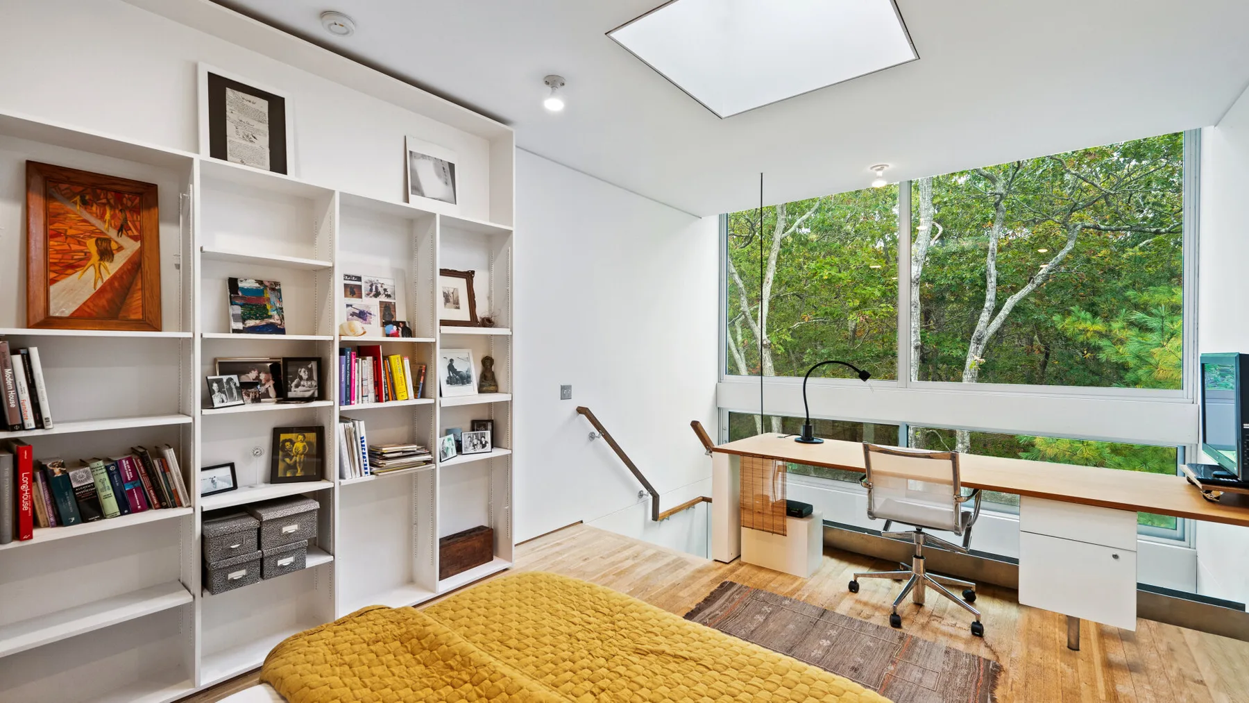 A bright bedroom with a bed, built-in shelving, and a desk by large windows.