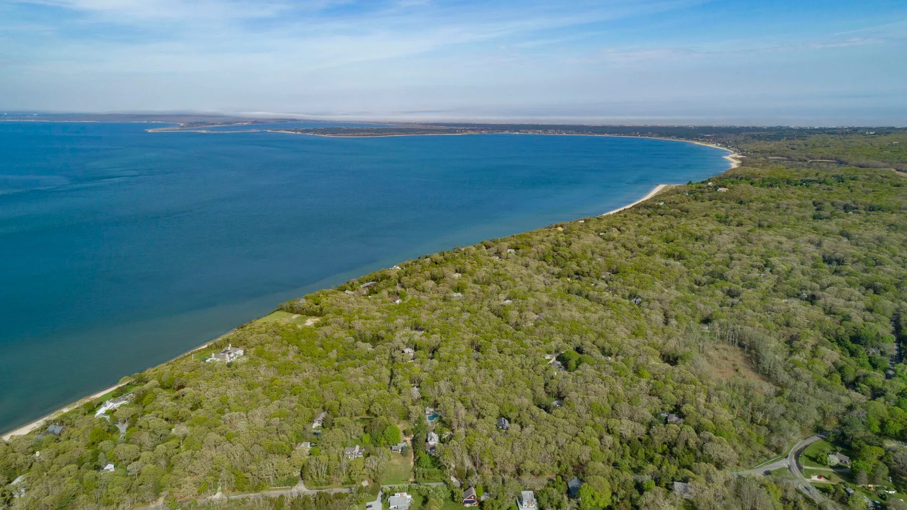 Aerial view of a wooded coastline beside a broad blue bay.