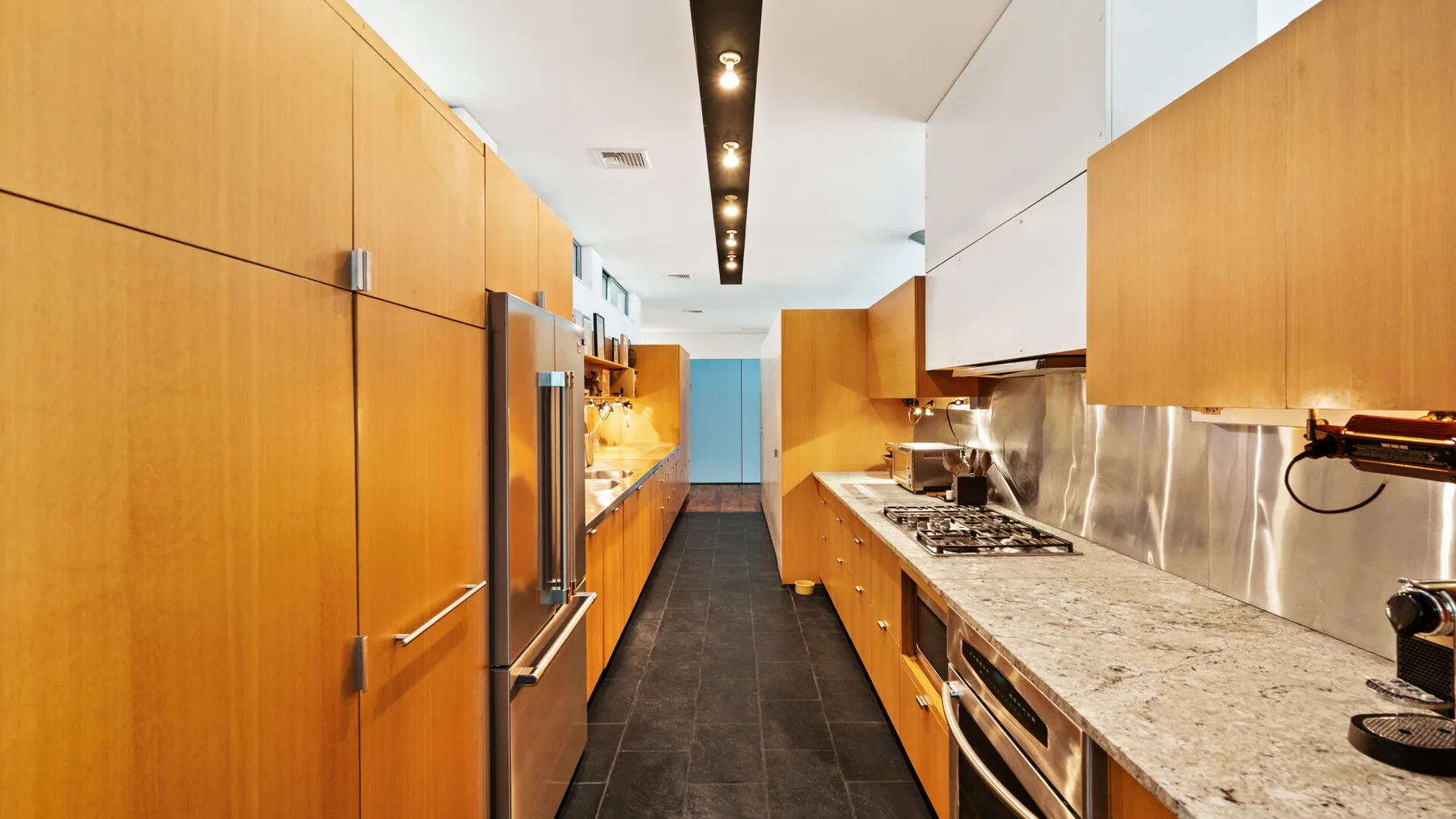 A long kitchen with wooden cabinetry, dark flooring, and a stone countertop.