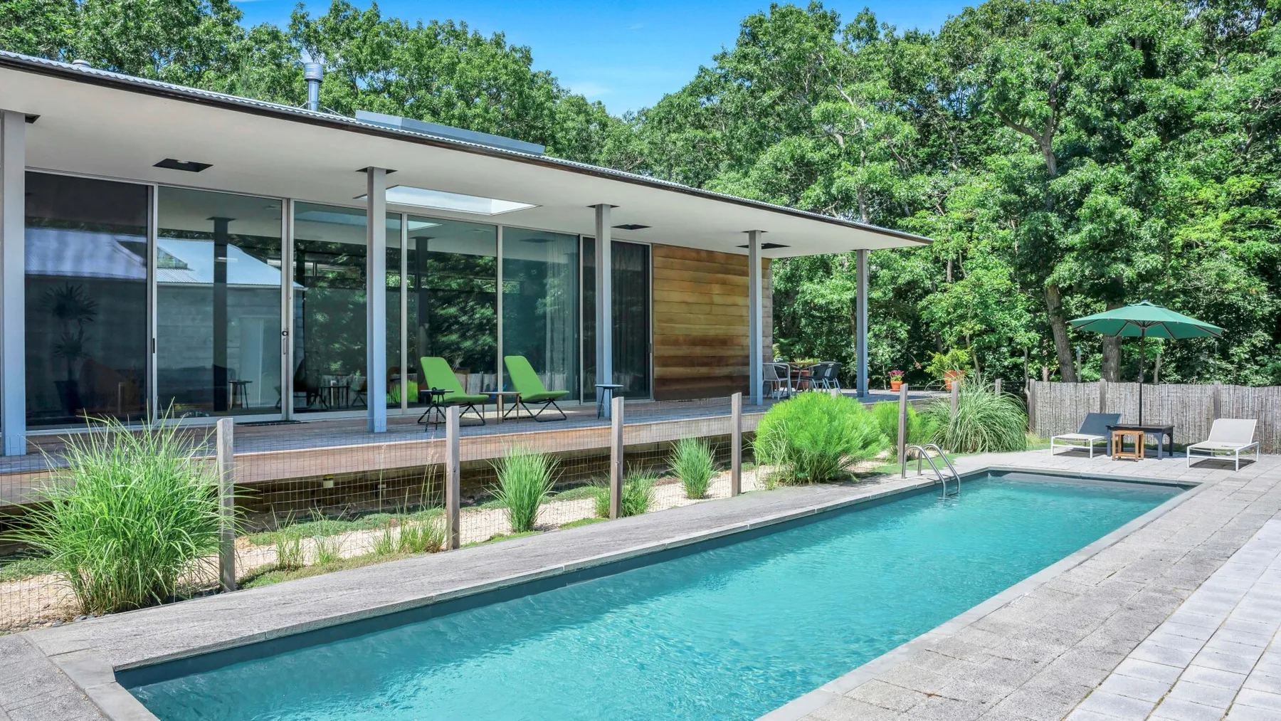 Una casa moderna se abre a una piscina y un patio ajardinado.