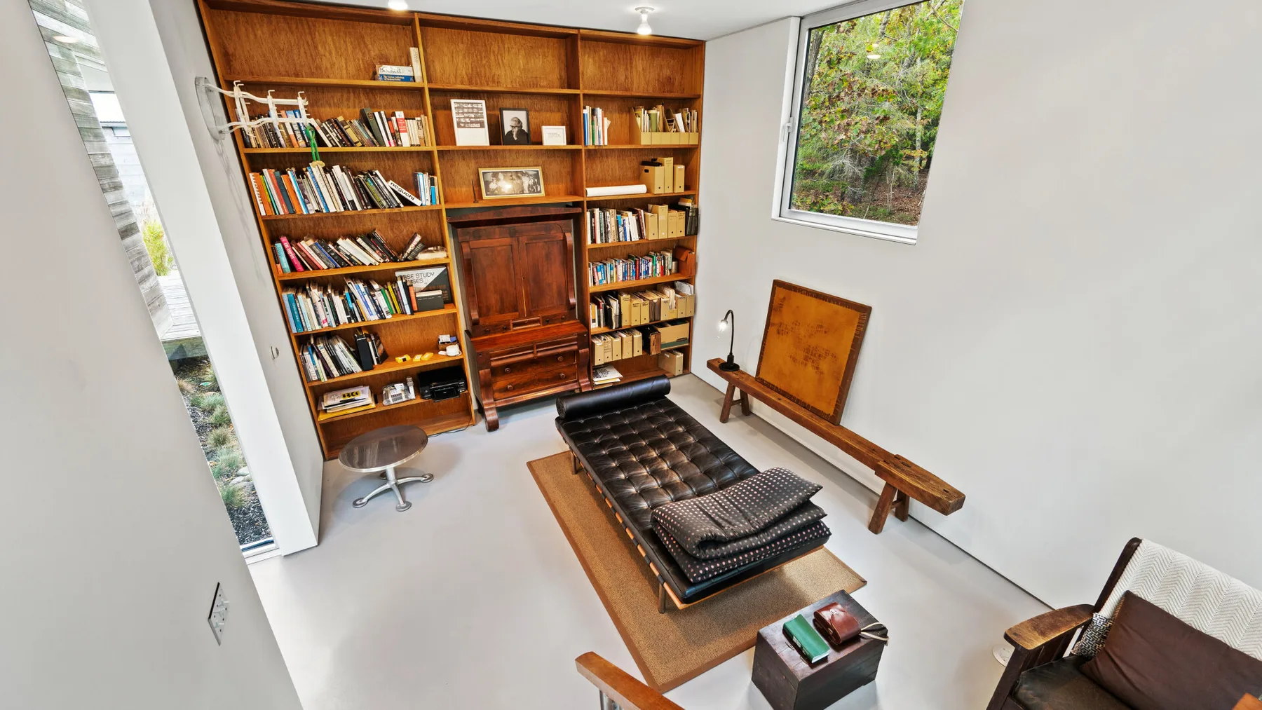 A bright reading room with a large wooden bookcase and a low daybed.