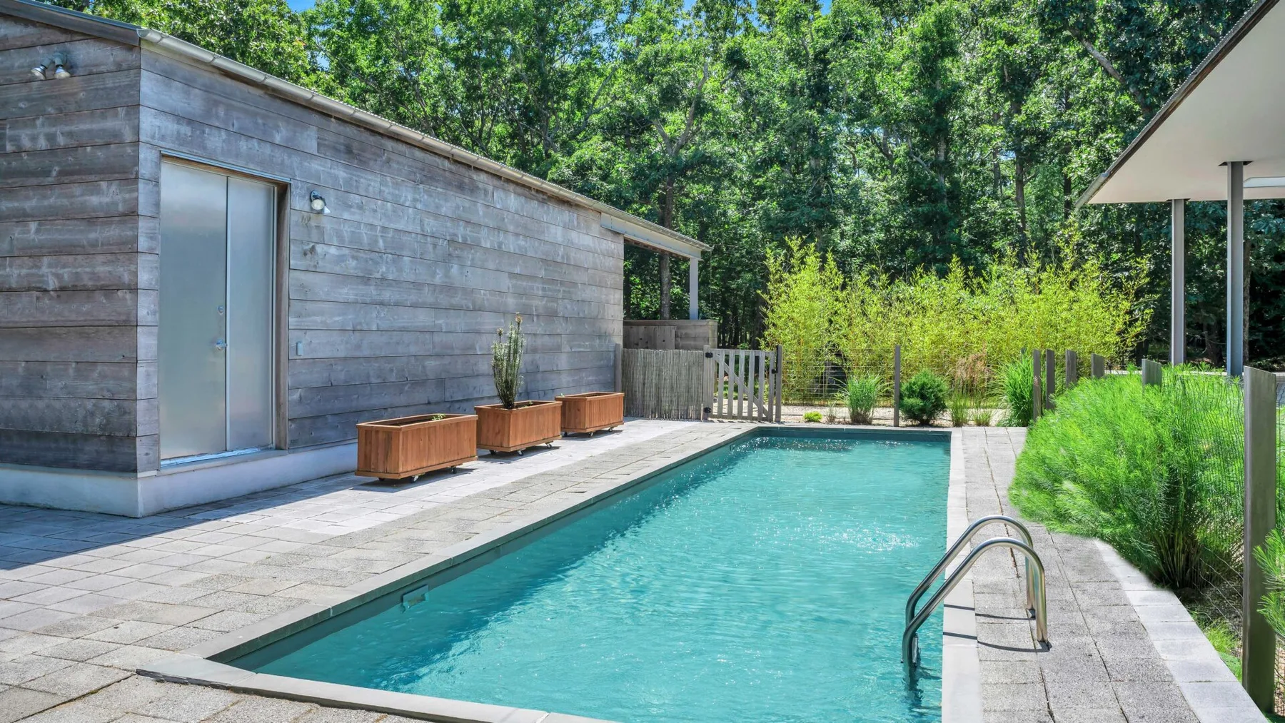 An outdoor swimming pool beside a modern building, with trees and greenery around it.