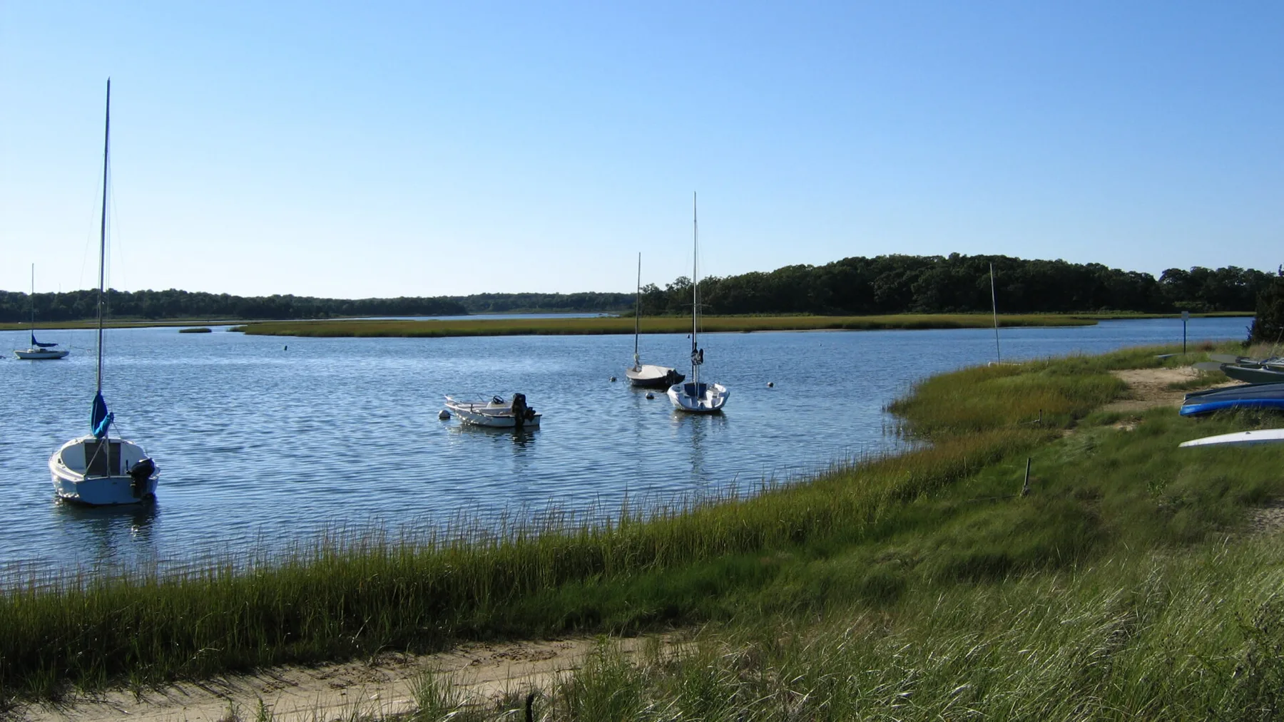 A calm waterway with small sailboats and grassy banks.