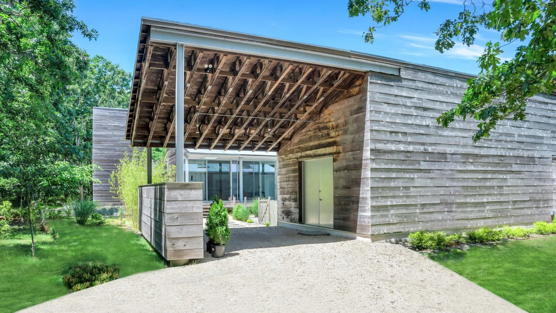 La entrada de una casa moderna da a un patio cubierto, rodeado de árboles y césped.
