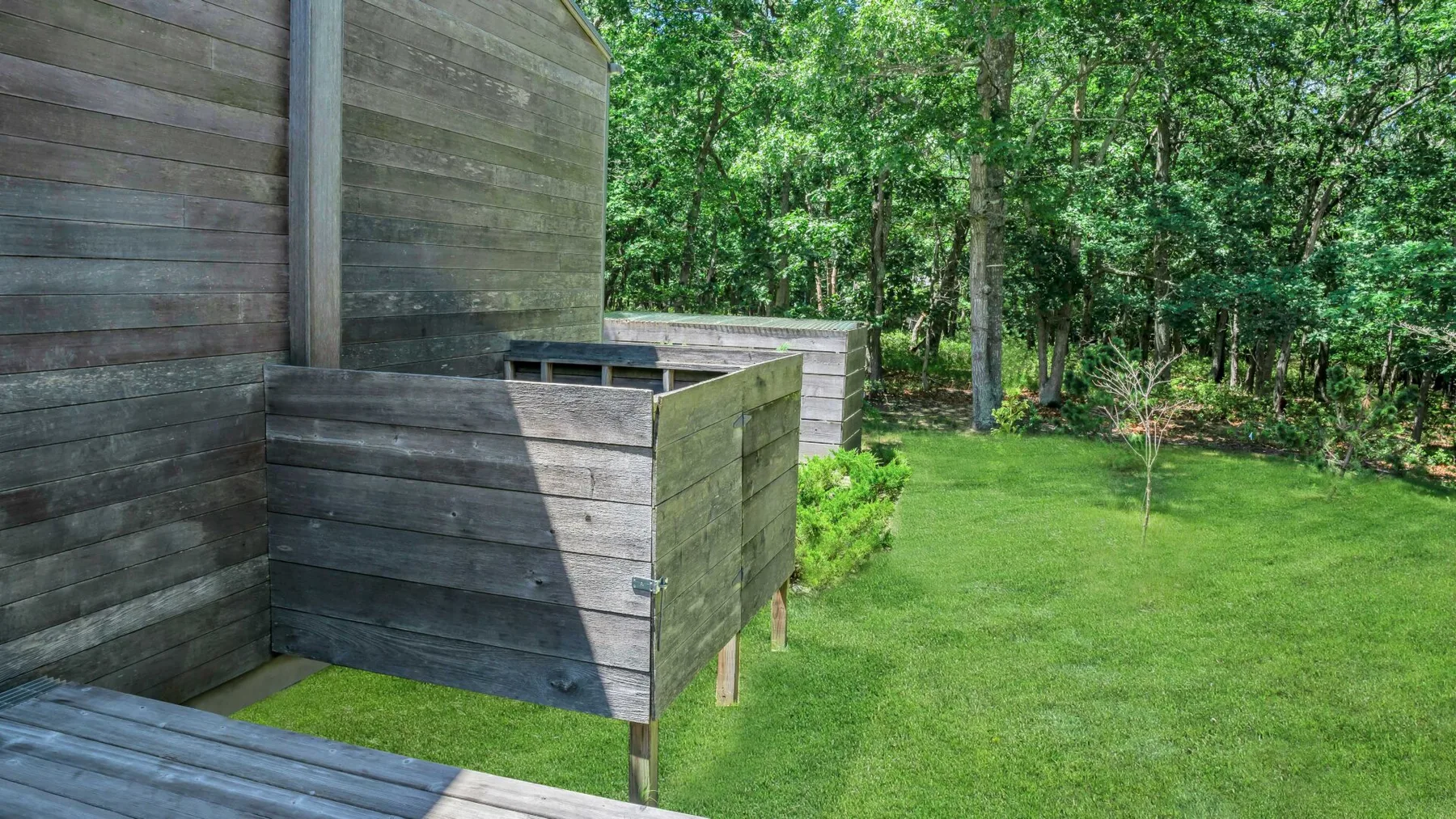 A grassy yard bordered by wooden fencing and leafy trees.