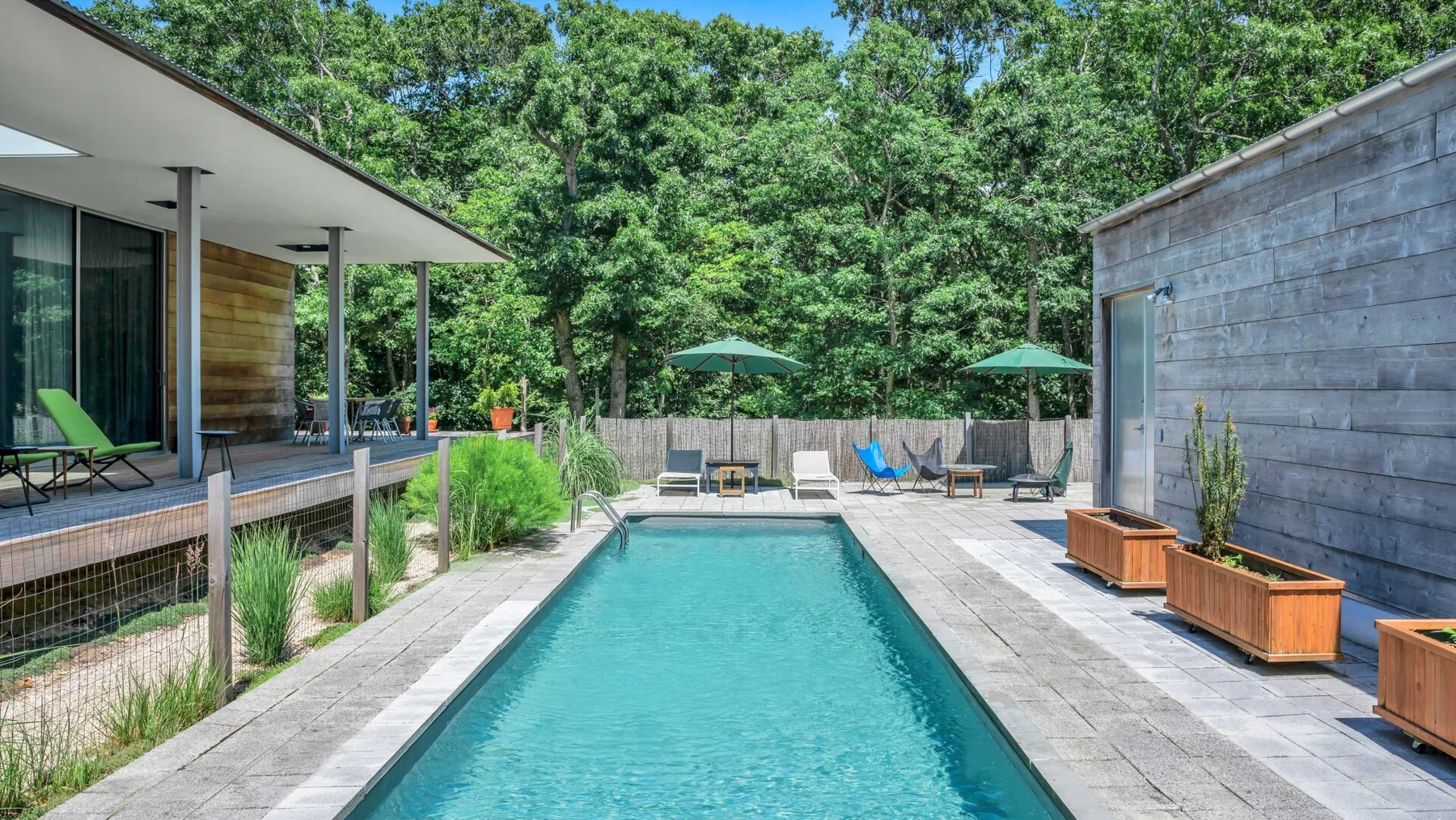 An outdoor swimming pool sits between a modern building and a wooden outbuilding.