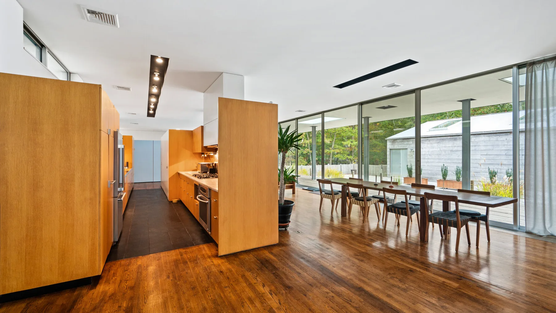 A modern kitchen and dining area opens onto a garden through wide glass windows.