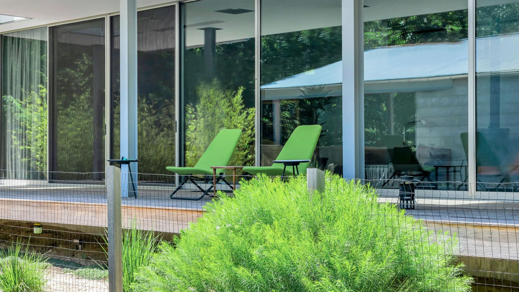 A modern glass-fronted building overlooks a deck with green lounge seating.