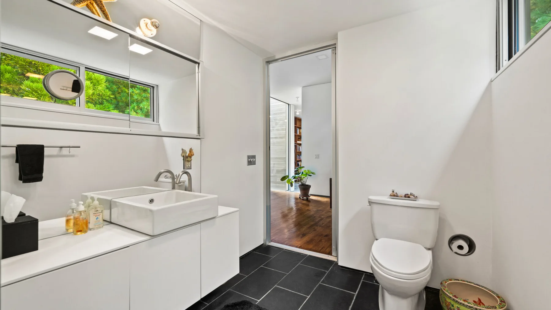 A bright bathroom with a white vanity and toilet beside an open doorway.